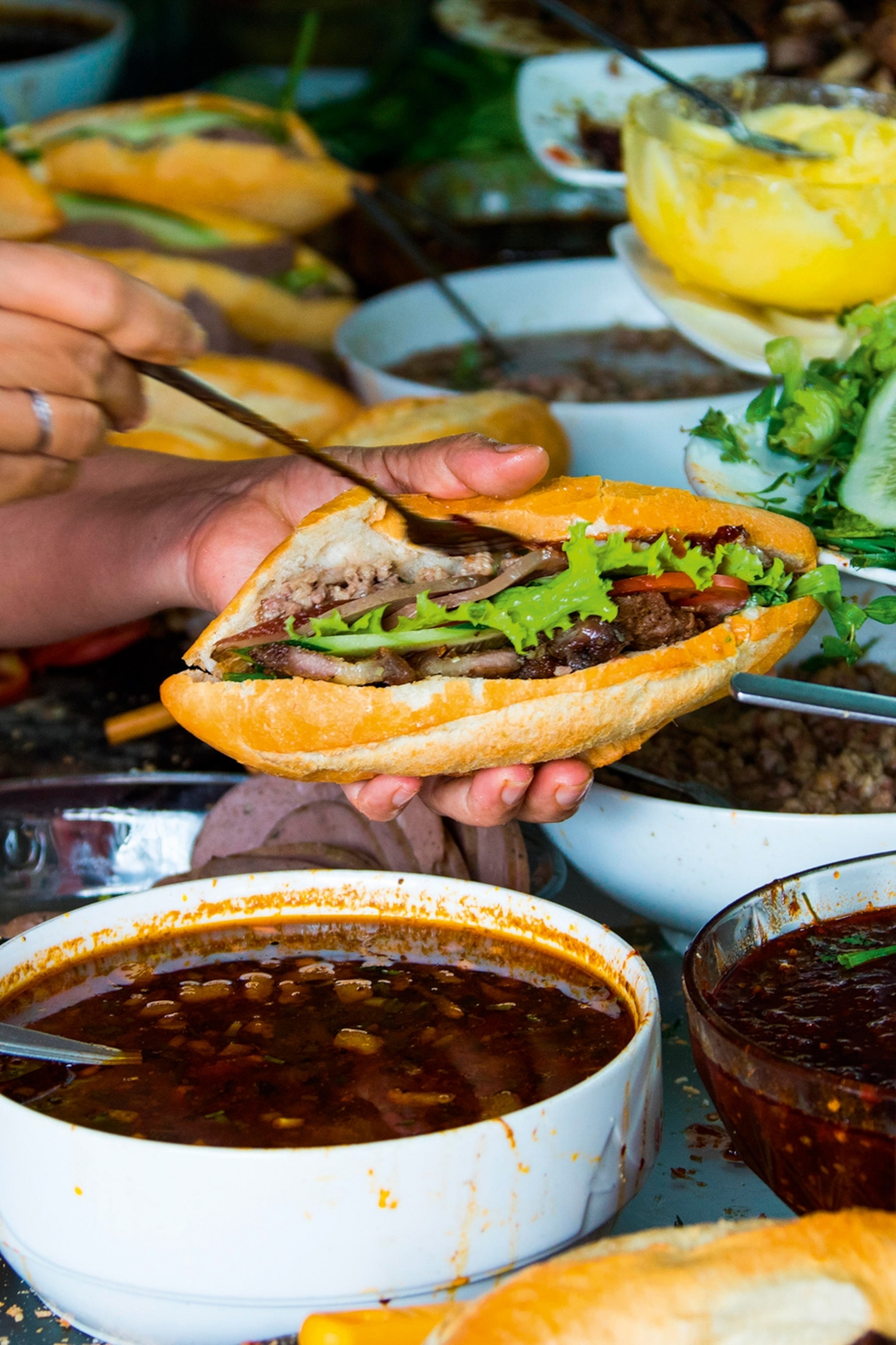 A person layering ingredients into a sandwich, including lettuce and a sauce.