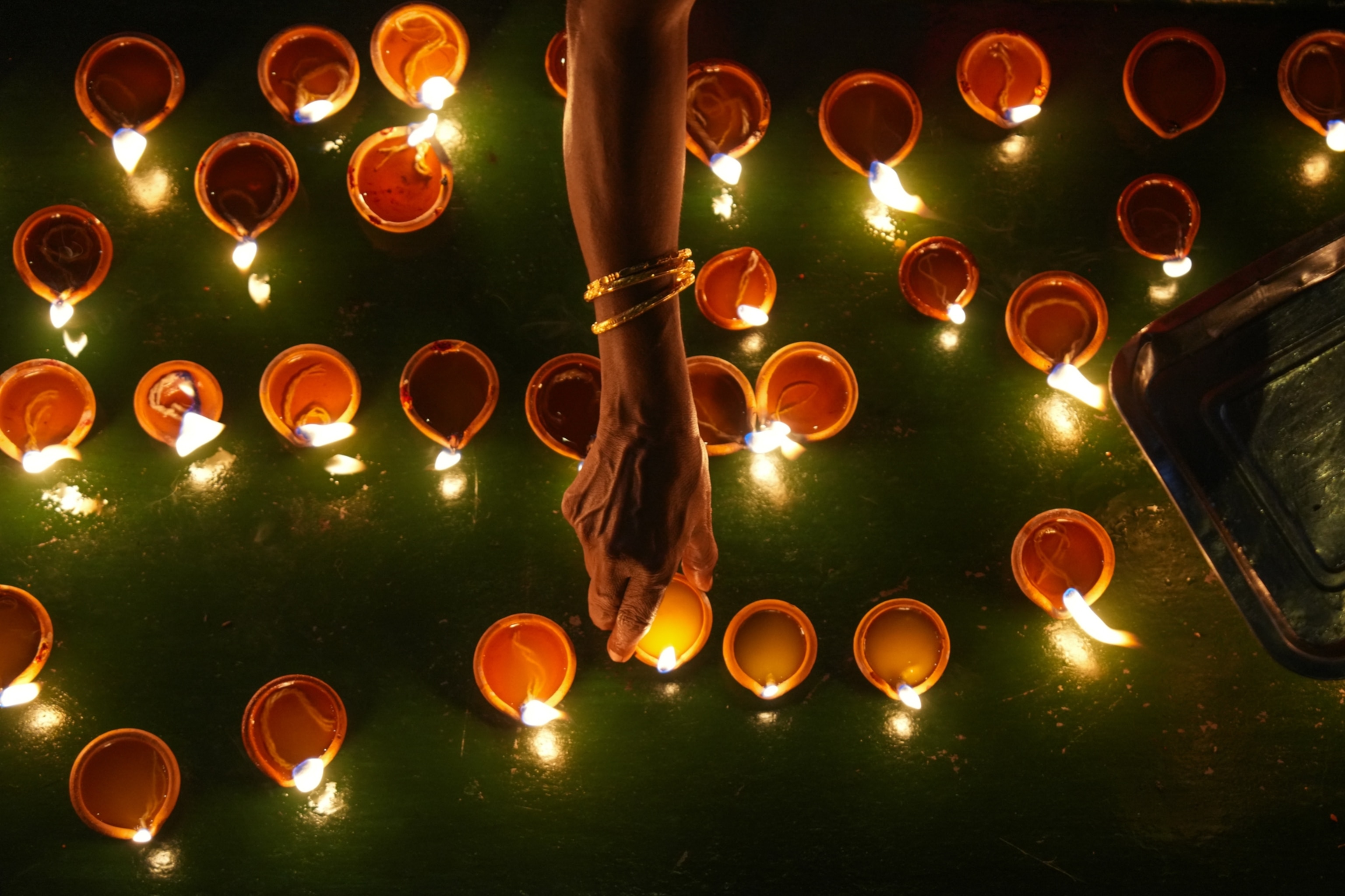 A hand places a lit oil lamp among others on a green surface