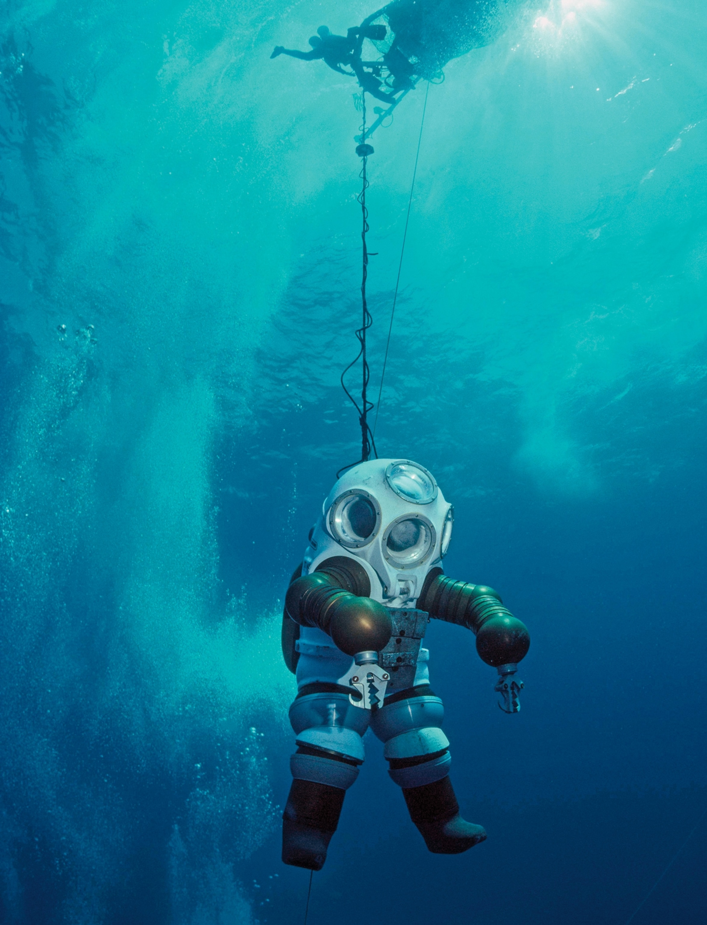 Person underwater in huge dry diving suit with four viewports.