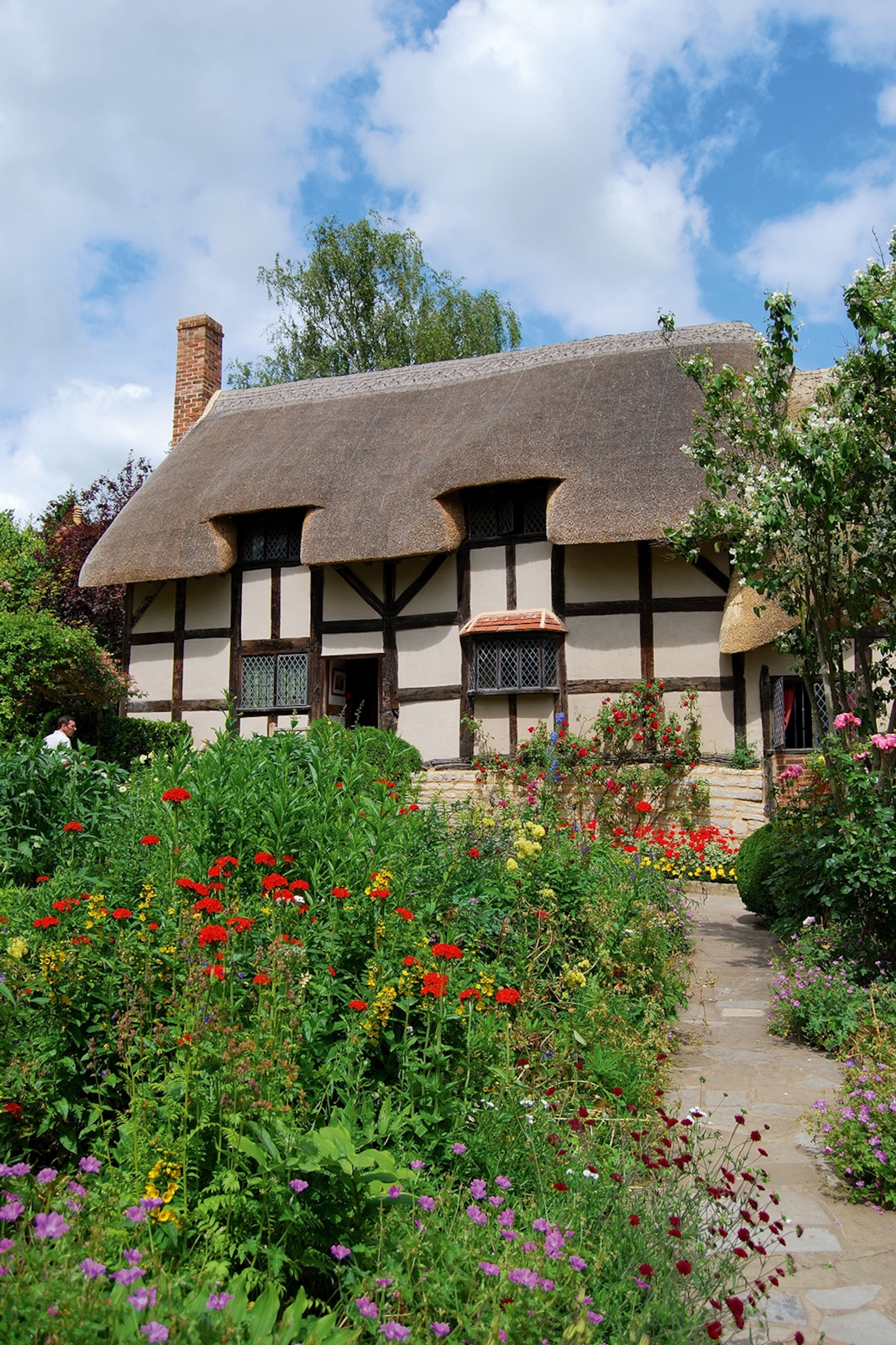 A medieval, English cottage surrounded by wildflowers and a bordering forest in summer.