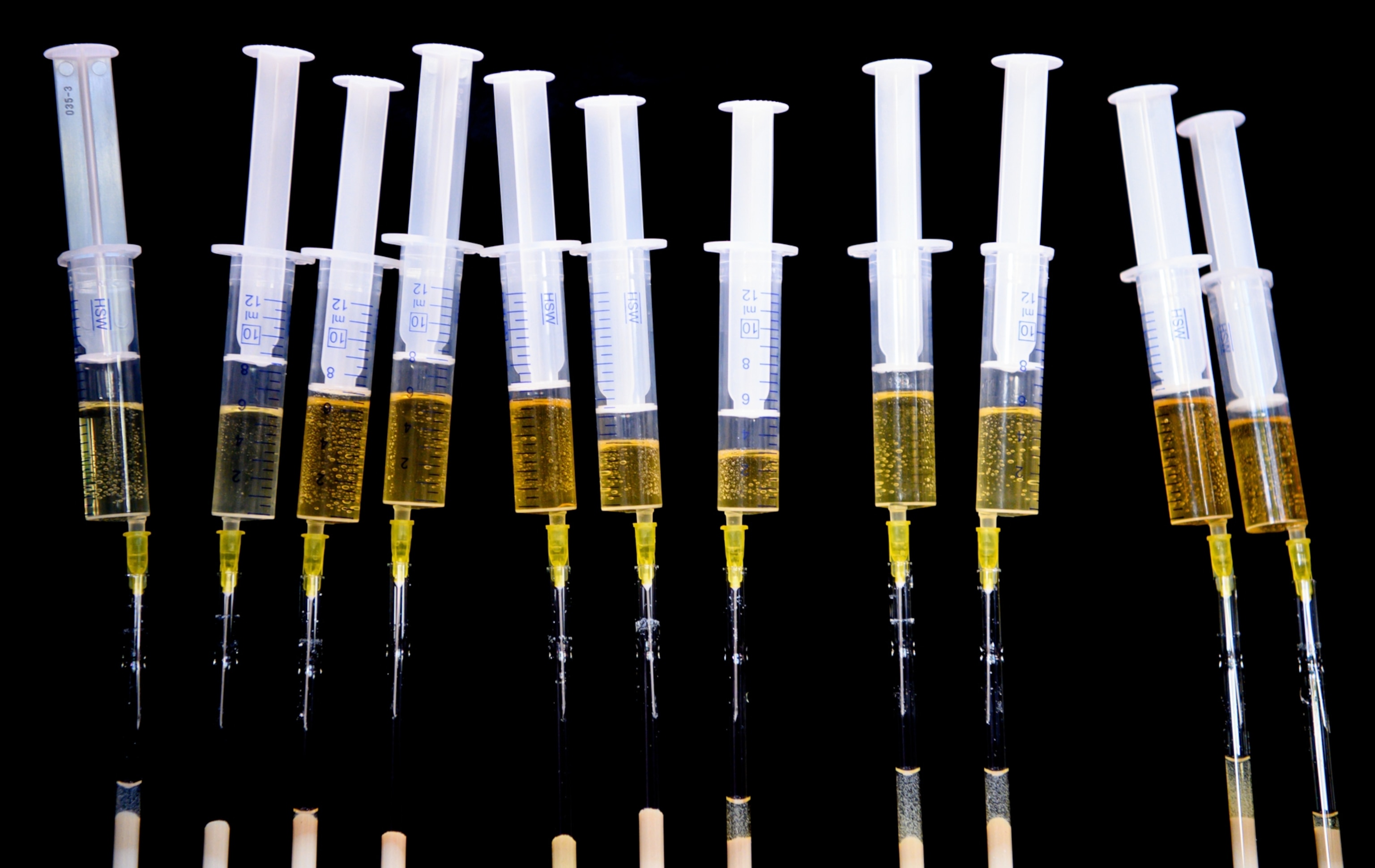 Several syringes filled with urine arranged vertically against a black background.