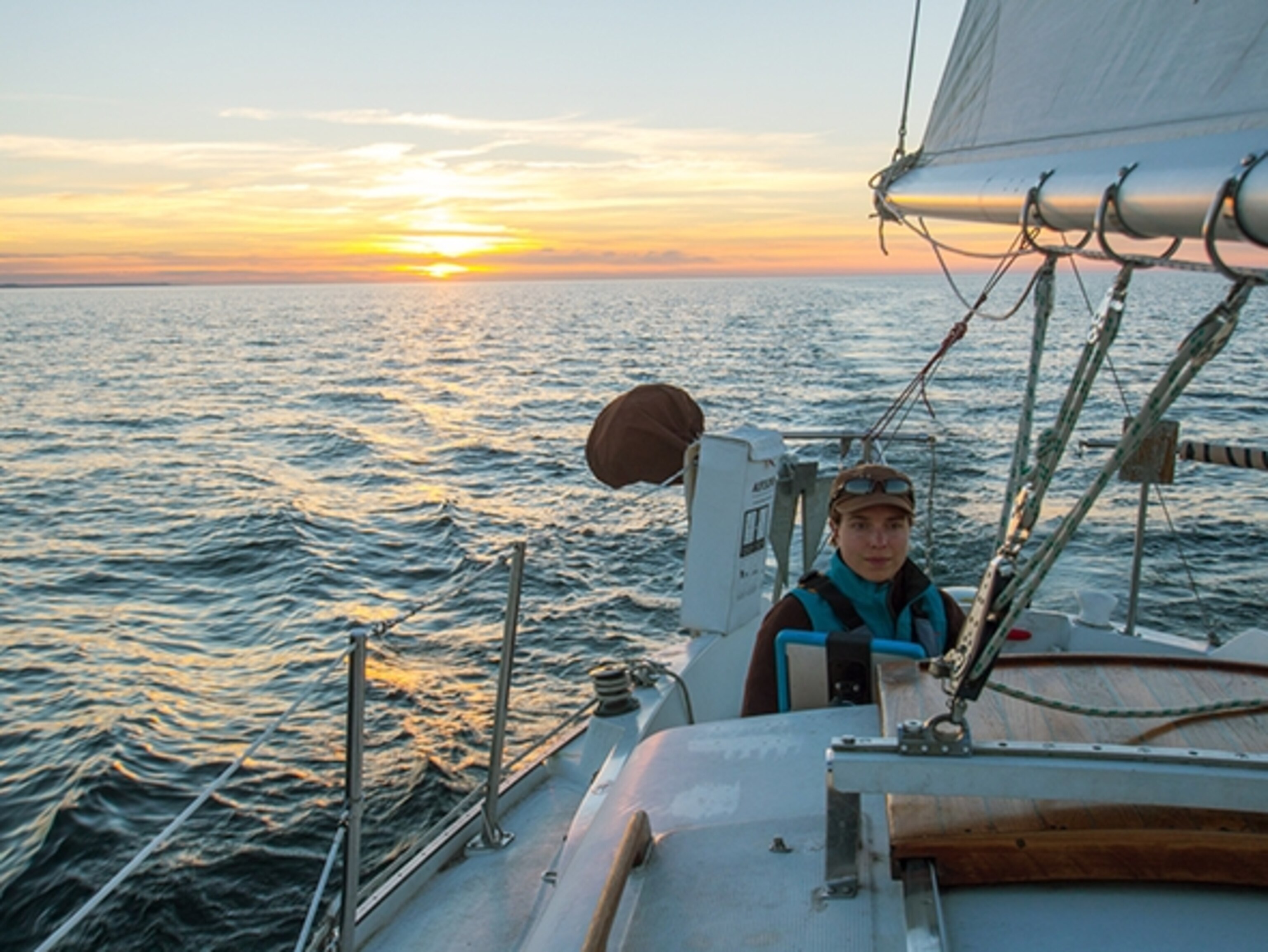 Amy Freeman sailing along the South shore of Lake Superior as the sun's warm rays appear on the horizon; Photograph by Dave Freeman