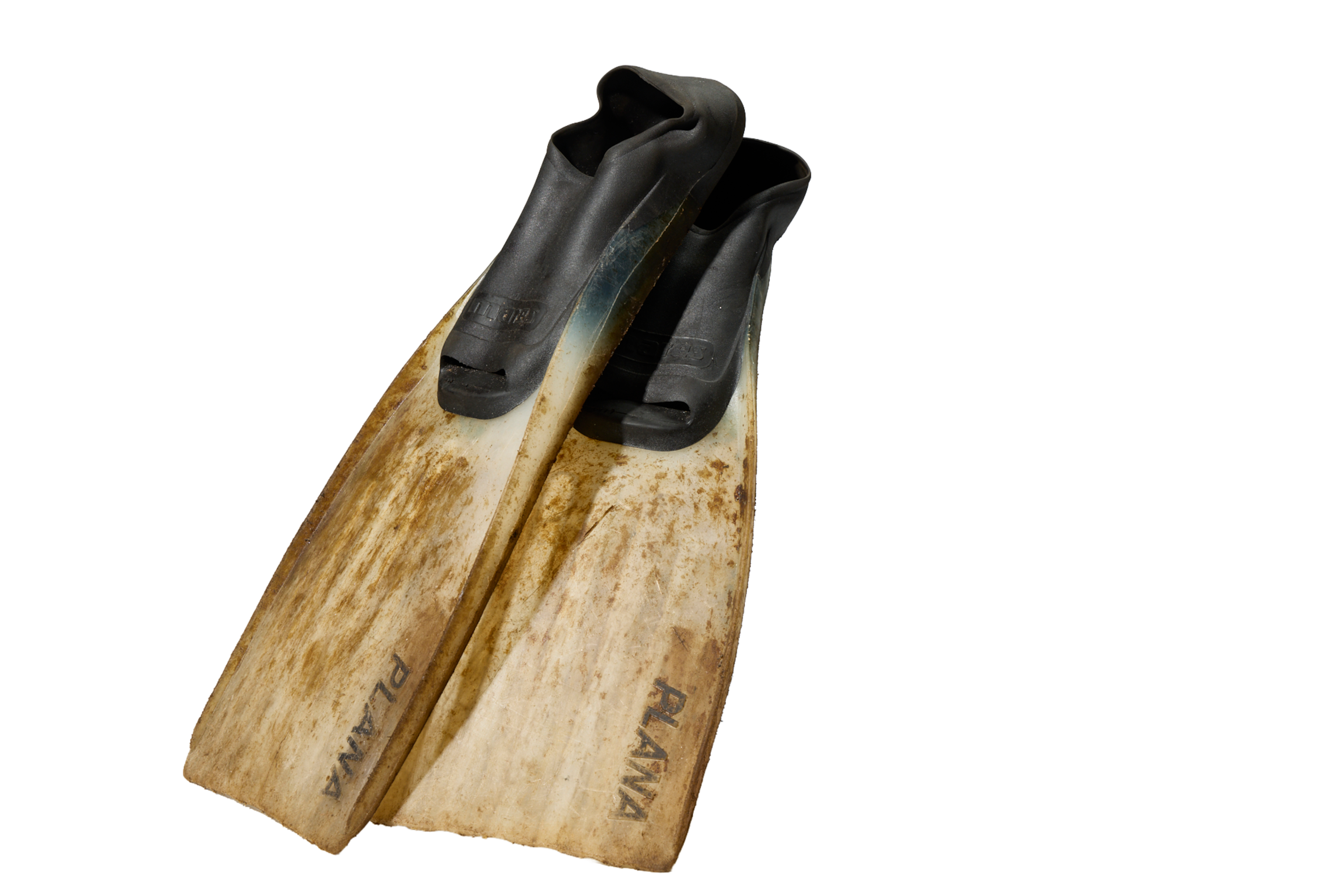Two worn swimming flippers. The slippers are black around the foot, and the extended flipper is white with brown marks from wear. One flipper is resting slightingly on top of the other and they are at a 45 degree angle towards the camera.