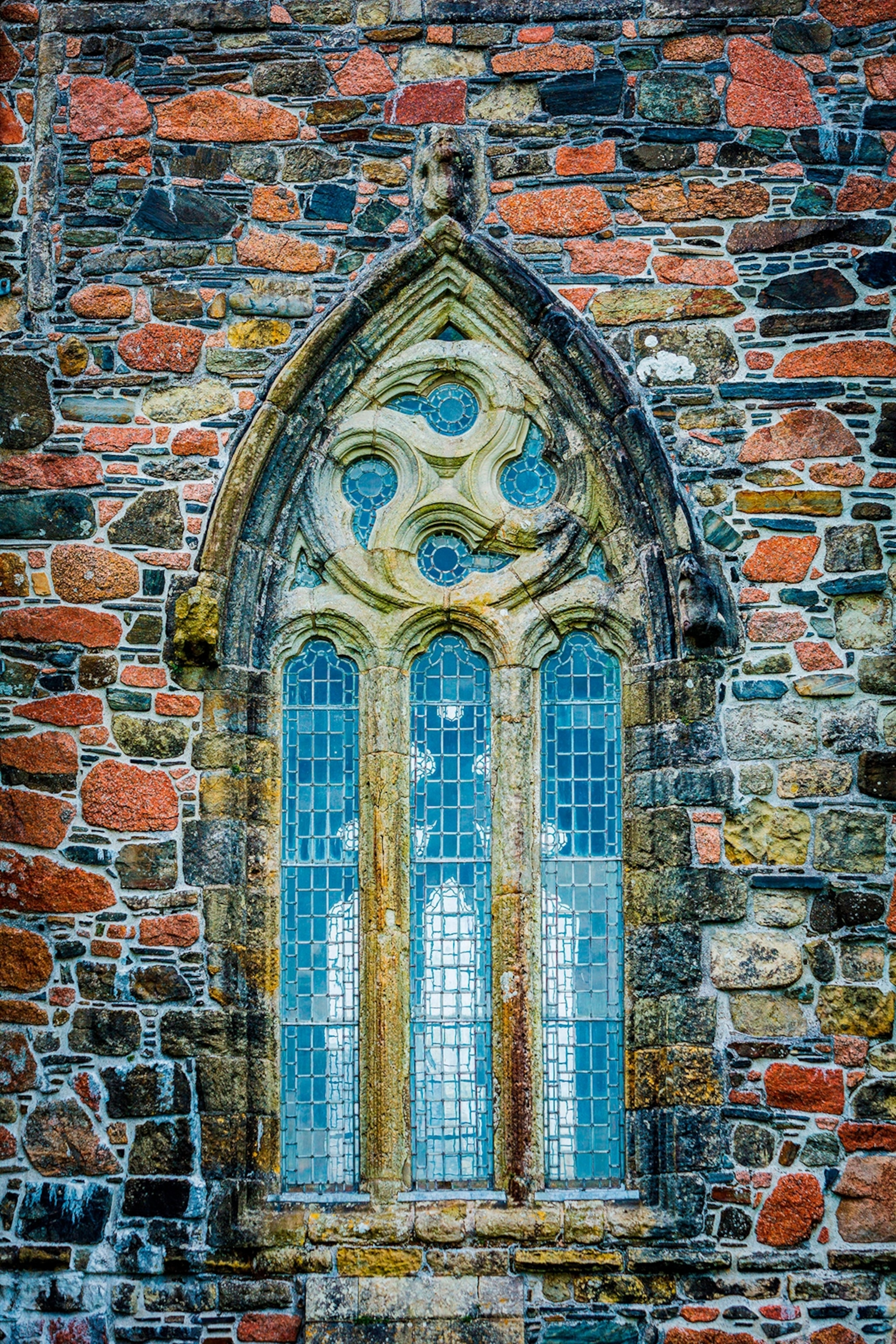 The exterior of a medieval abbey focusing on a pointed, tall window with swirled stone elements.