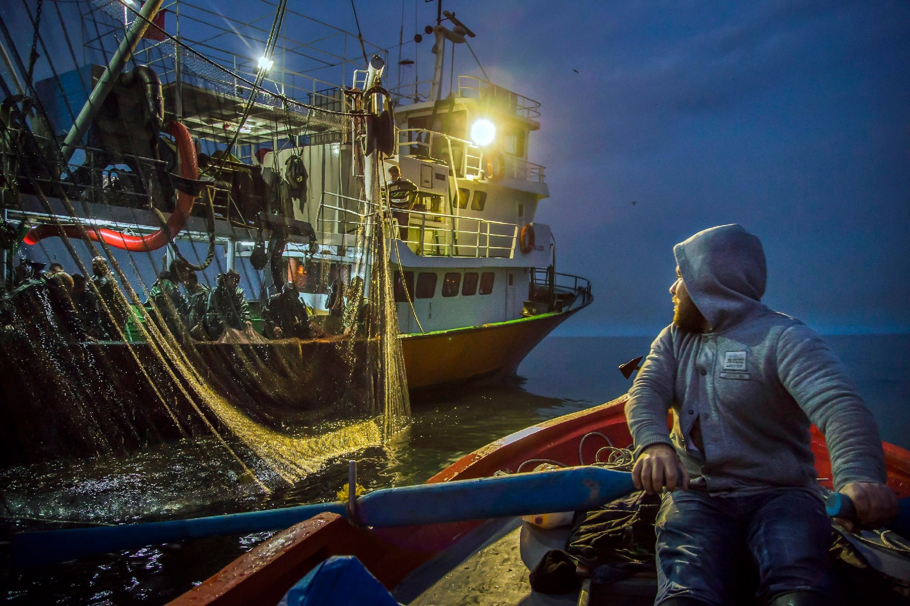 fisherman in small boat next to big boat