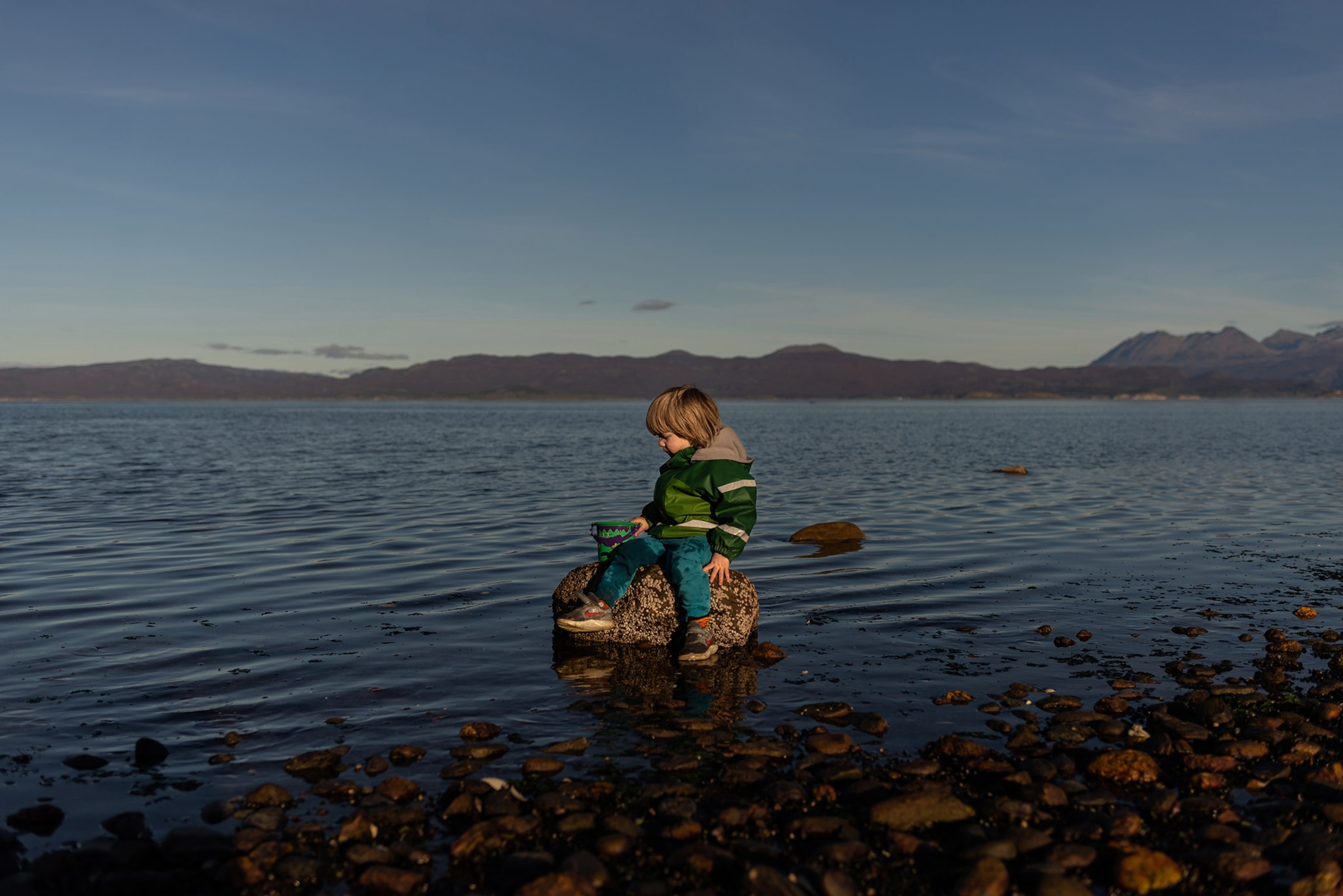 a little boy sitting on a rock in the middle of the ocean