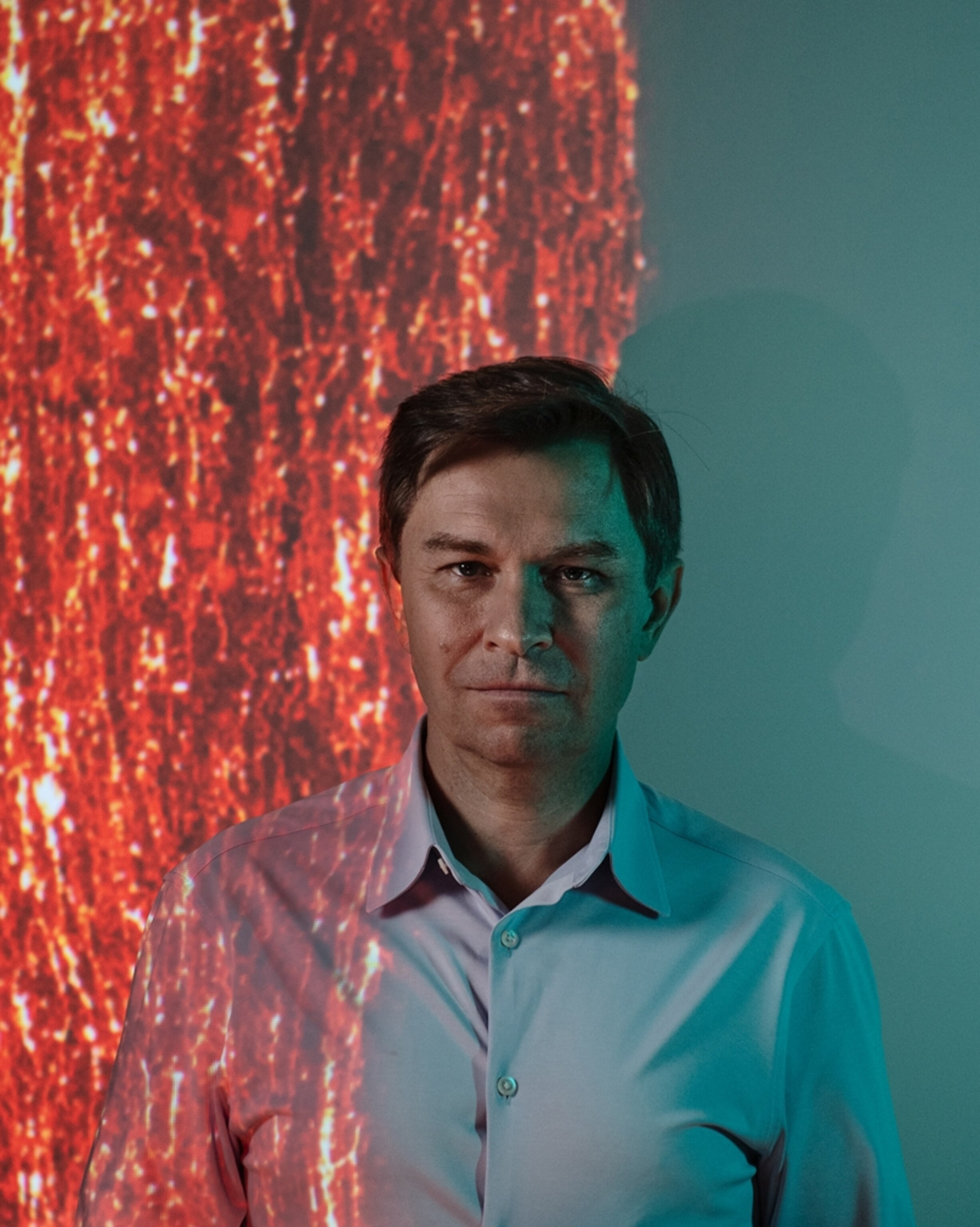 A portrait of a man who stands in front of a projected image.