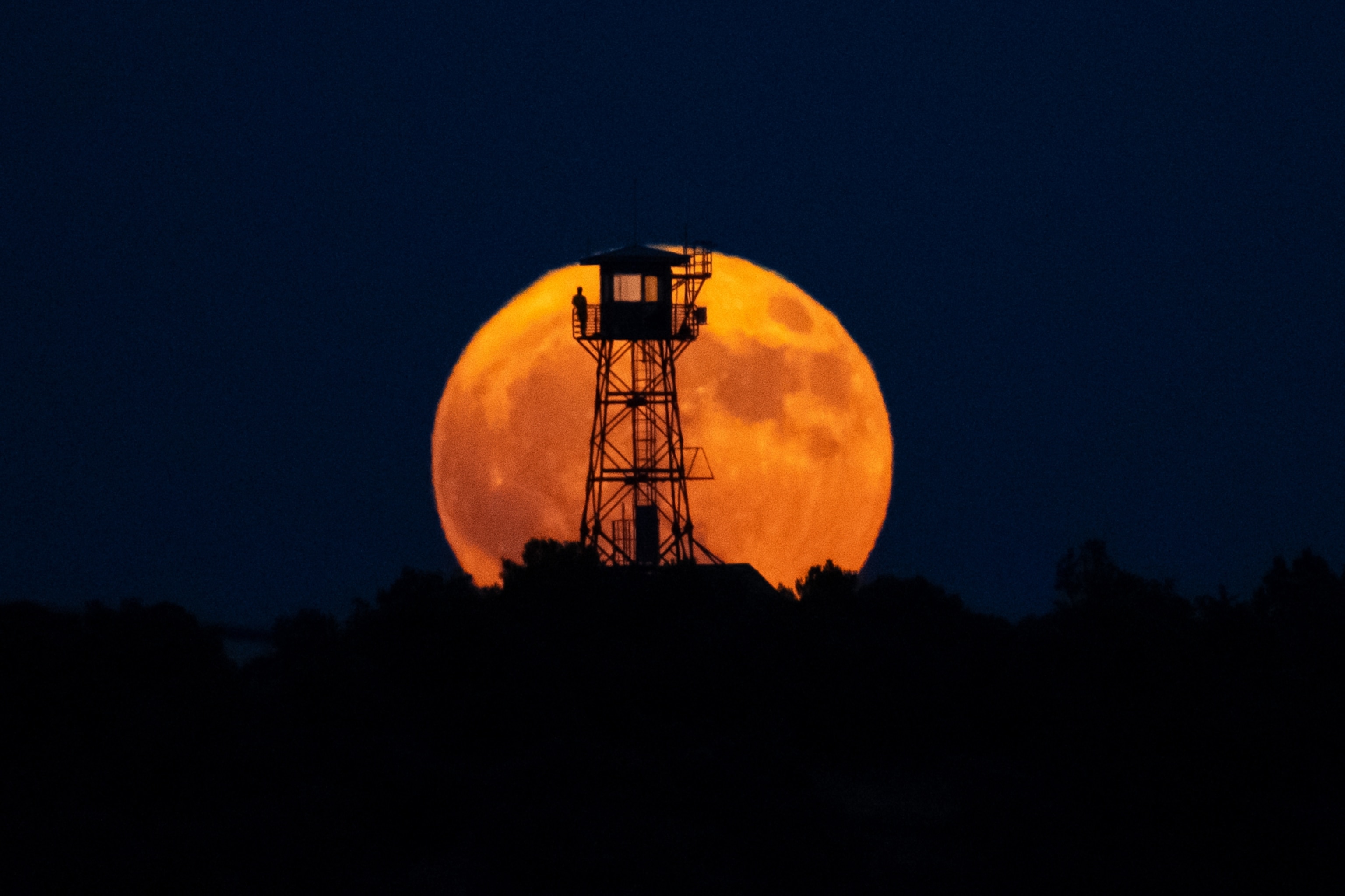 A large orange moon rises behind a silhouetted lookout tower