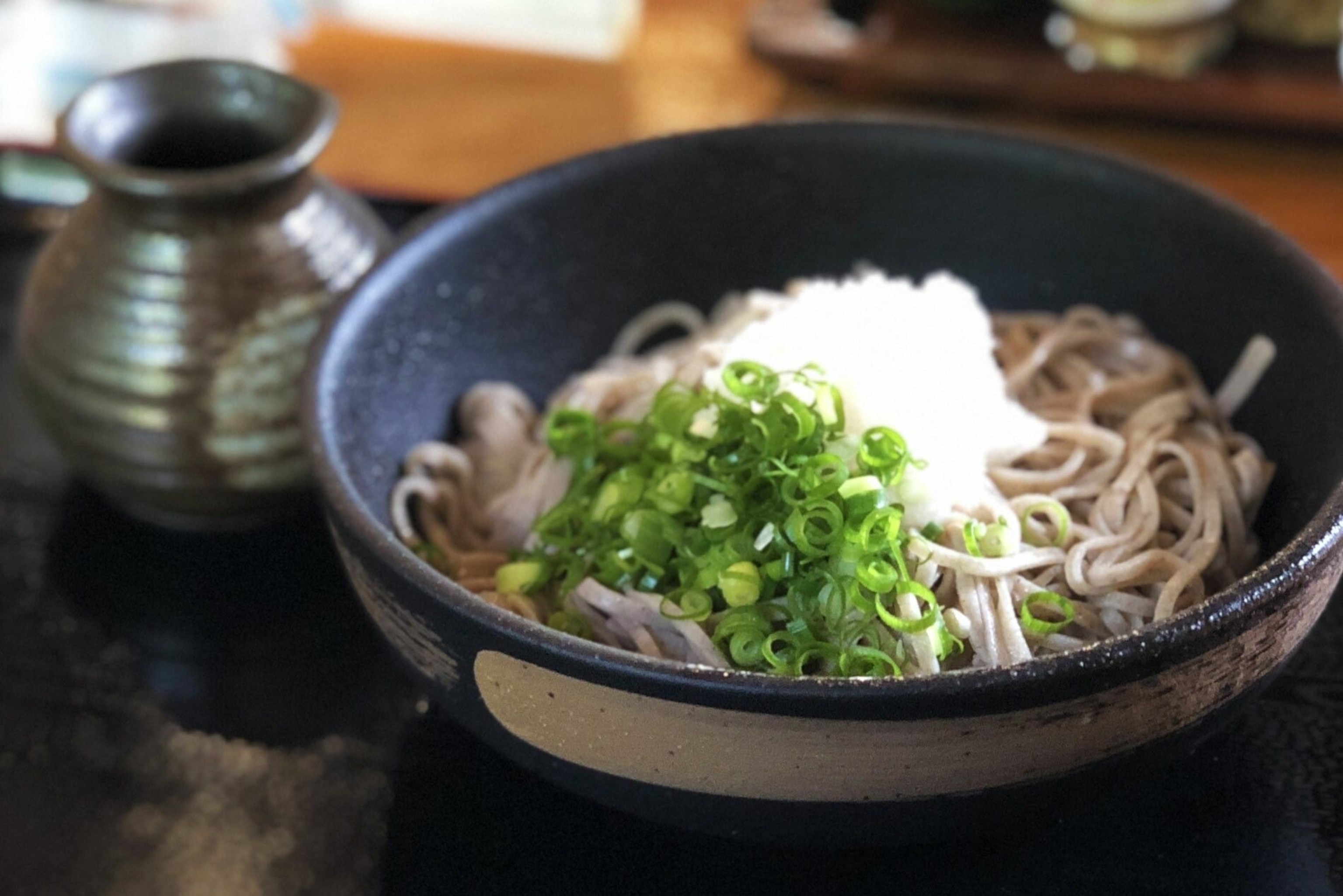 A bowl of soba - noodles topped with green spring onions.