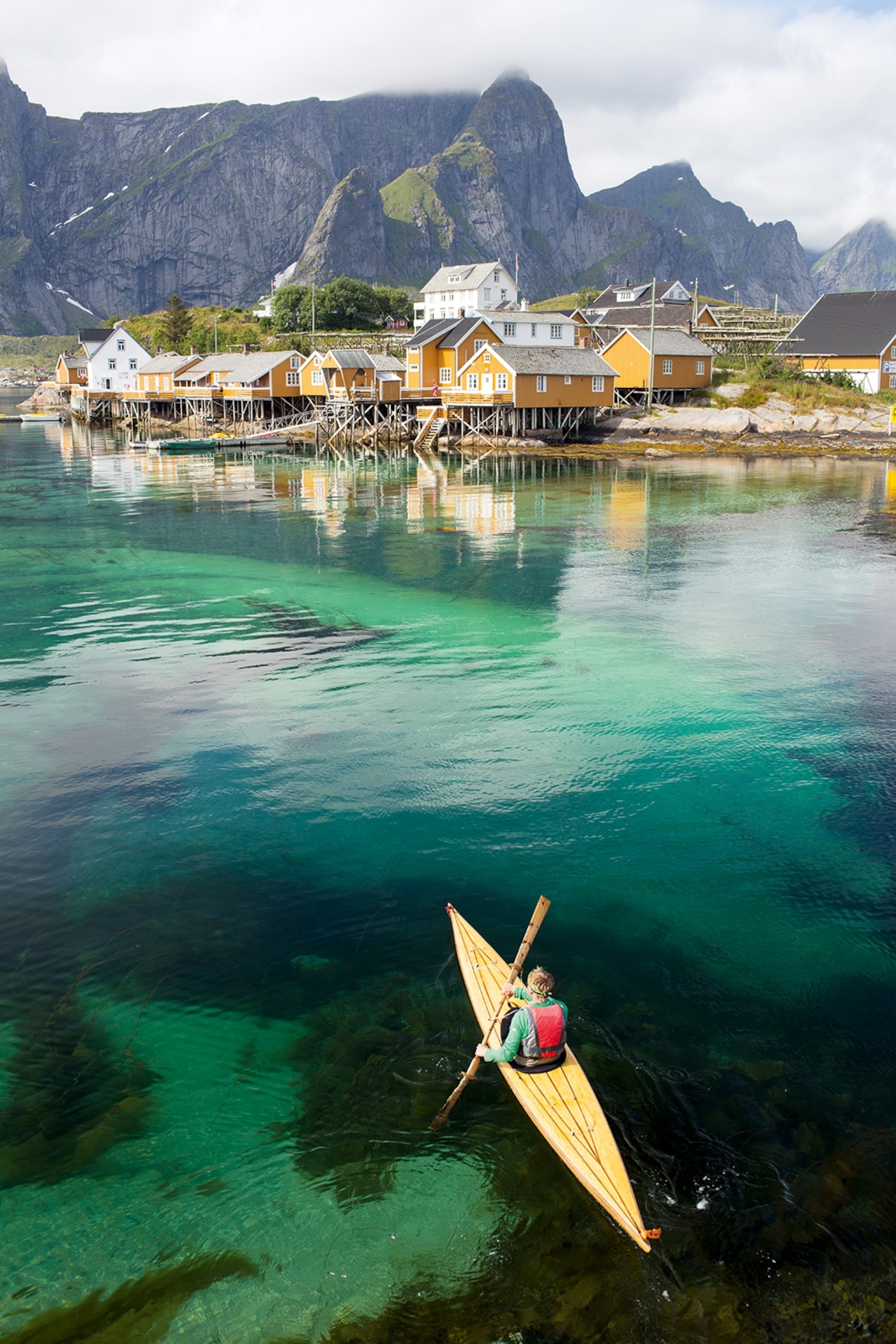 Clear waters on the coast of a rugged island with houses as a kayak paddles towards them.