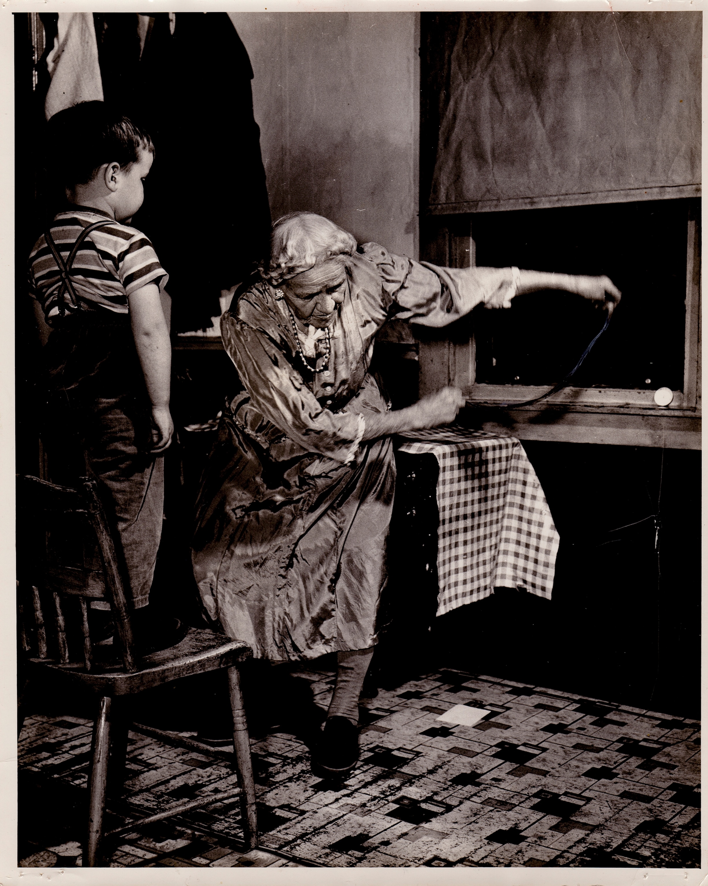 An elderly woman stands in a kitchen with a young boy