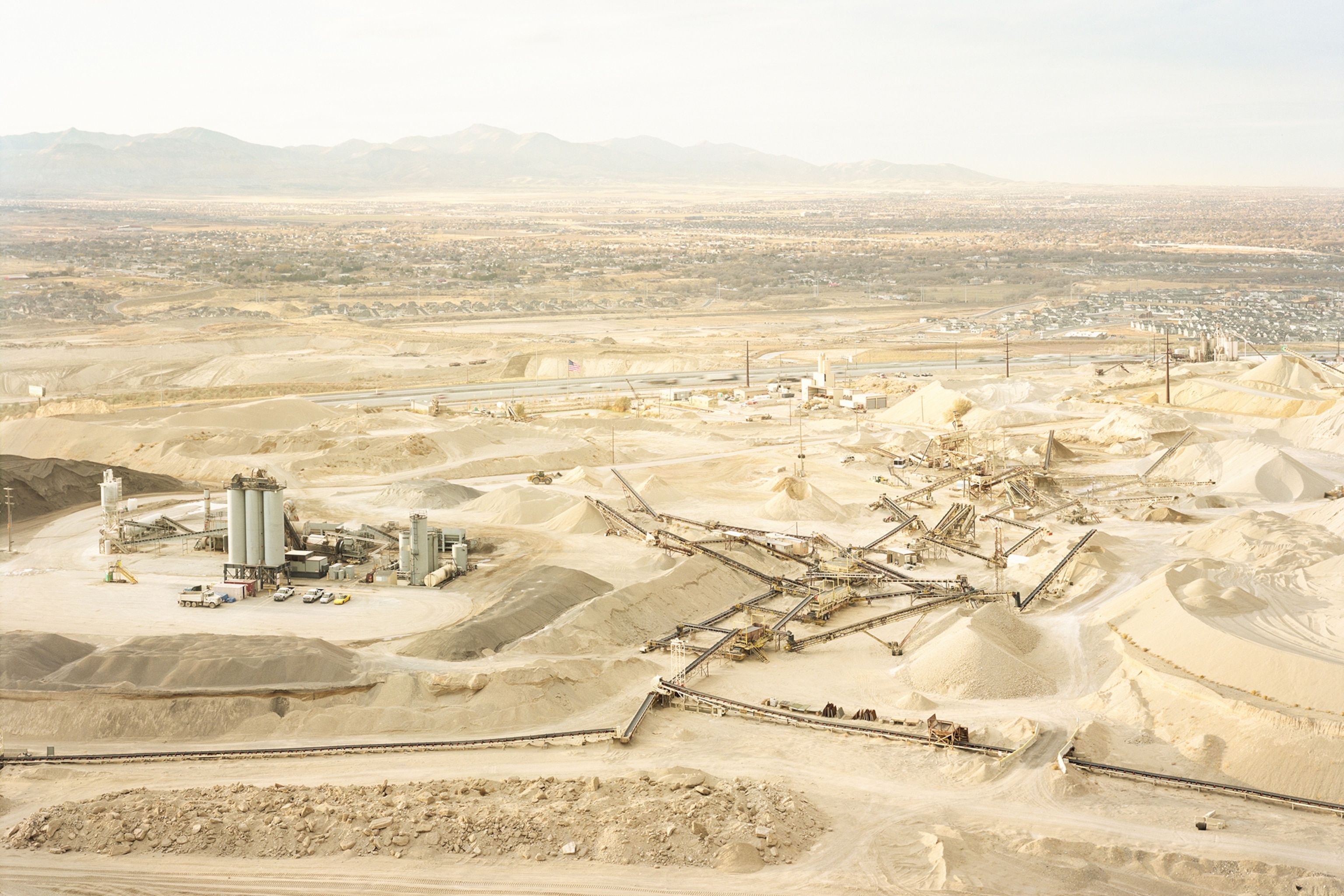 A processing plant sits amongst several large industrialized gravel pits, with many suburban homes in the distnace.