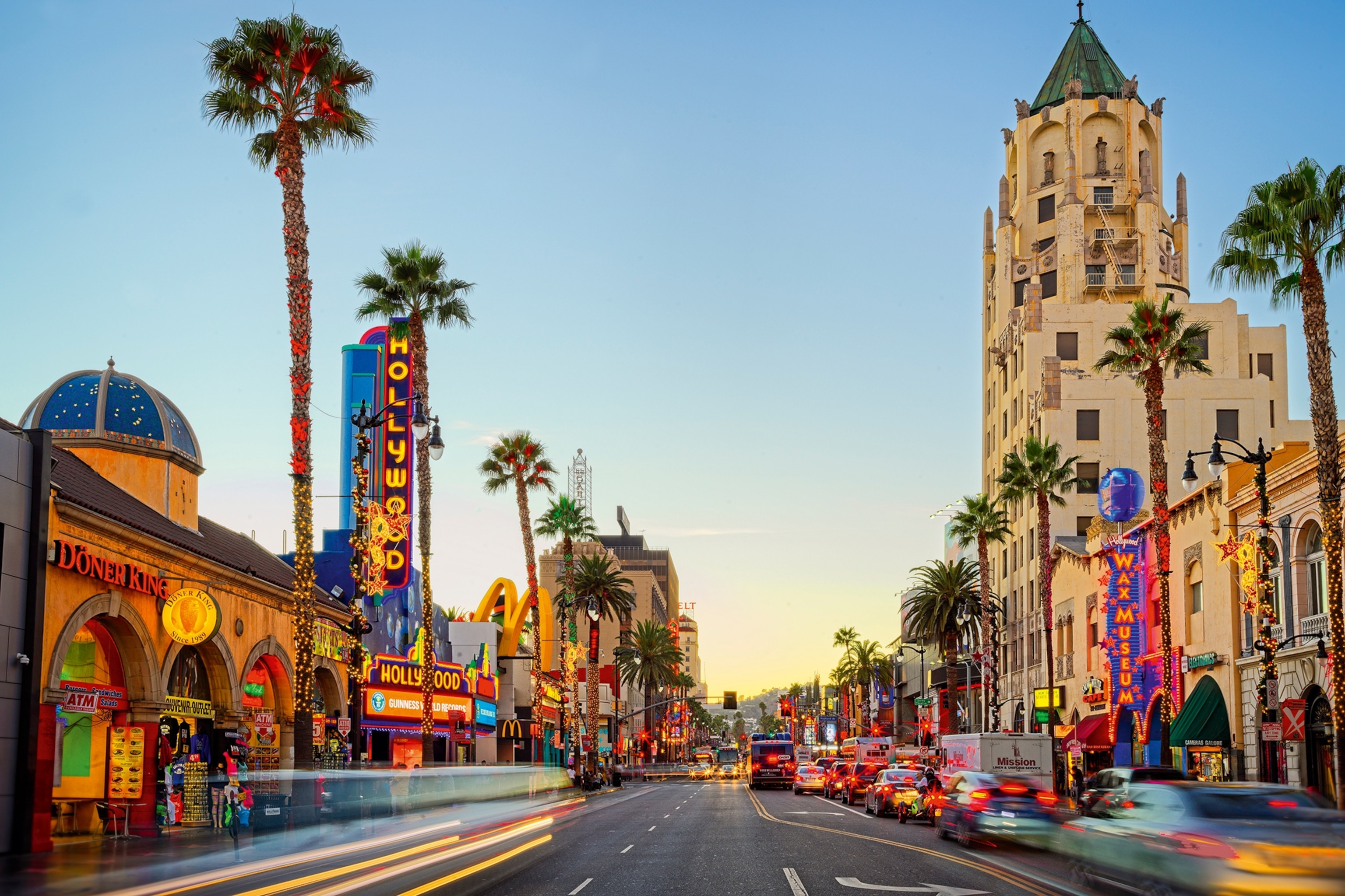 A busy boulevard with palm trees and neon signs at dusk.
