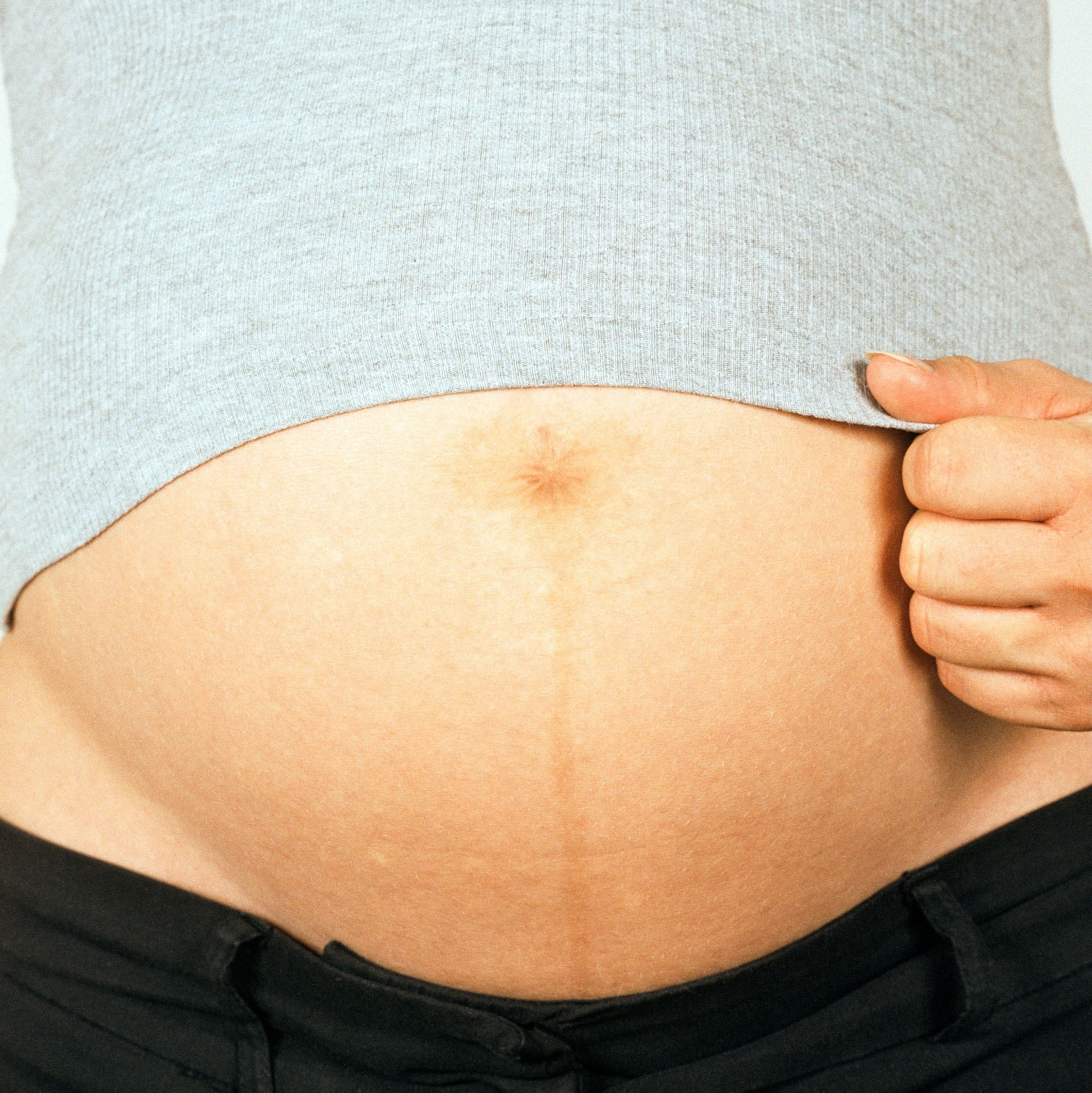 Close-up of a pregnant belly with a light gray shirt slightly lifted, revealing a prominent belly
