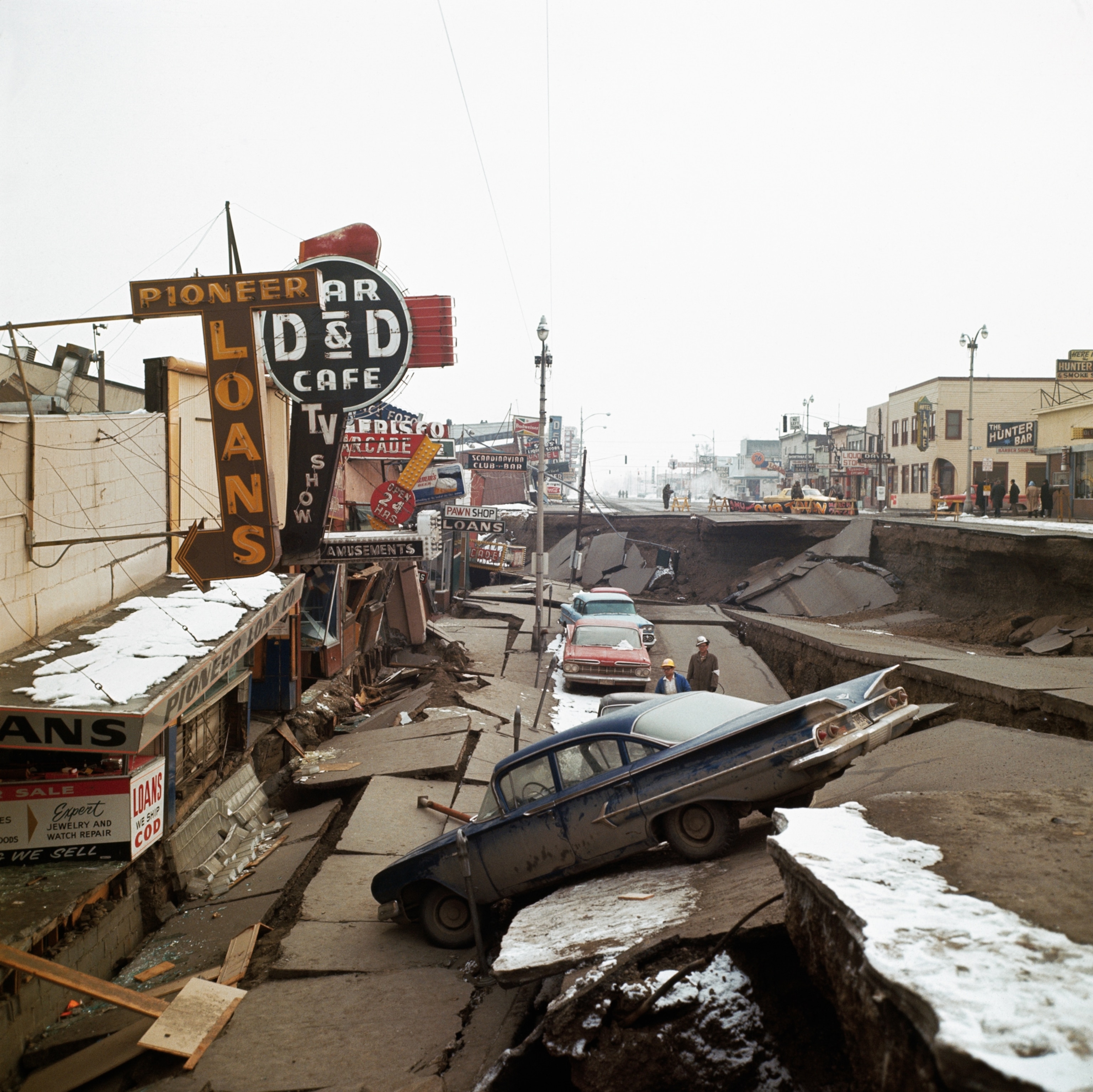 Damaged storefronts and cars along a caved-in street following an earthquake