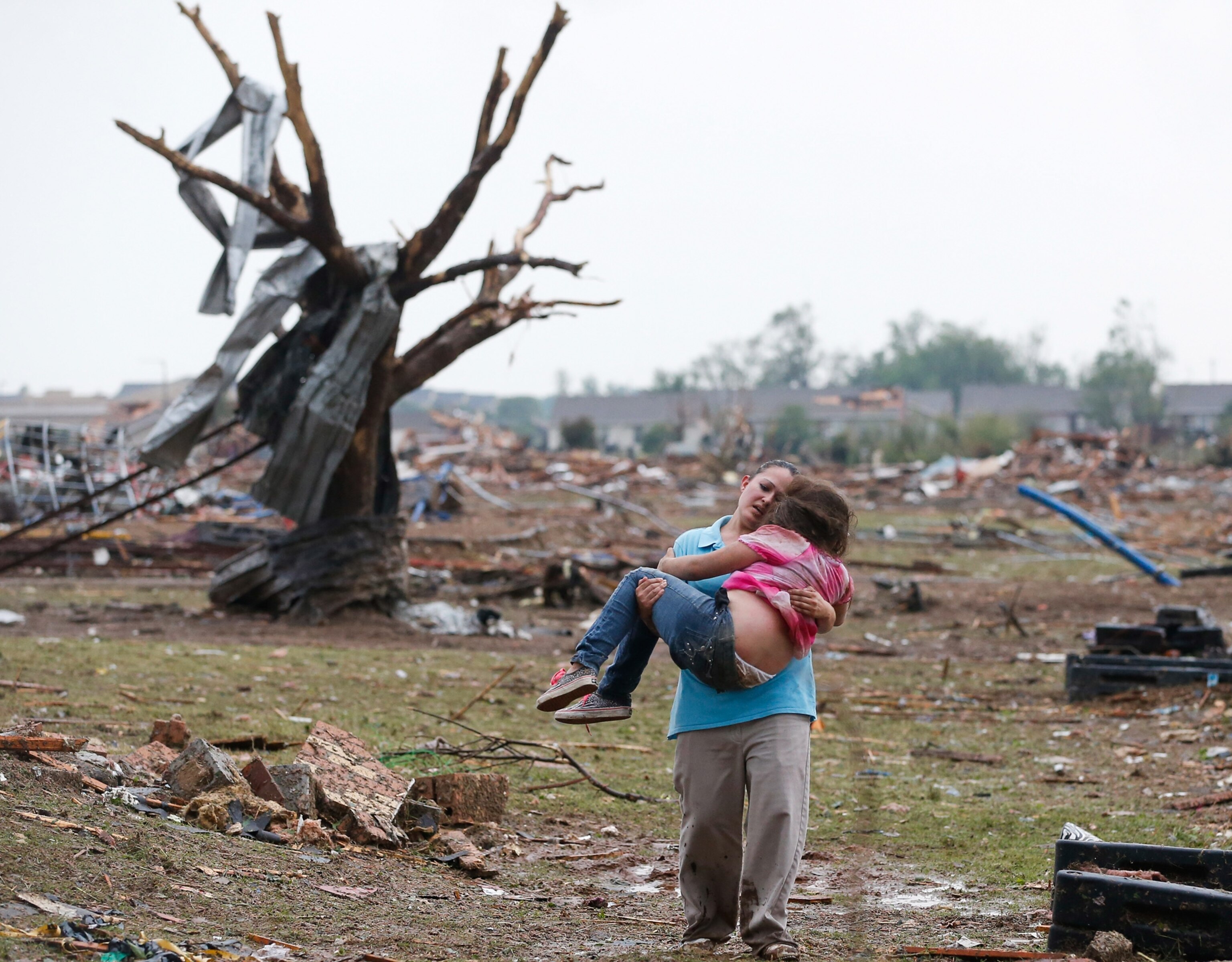 a woman carrying a child through tornado damage, Oklahoma.
