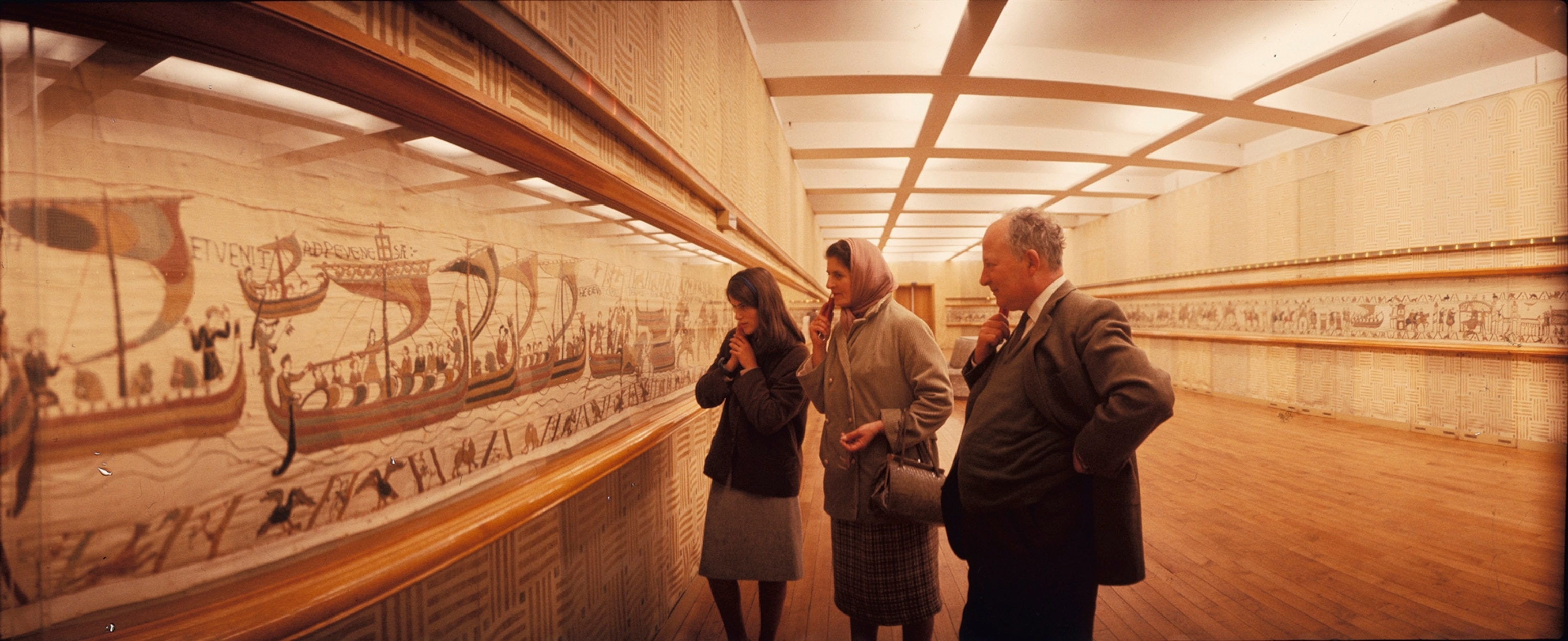 Visitors listen to commentary as they examine the Bayeux Tapestry.