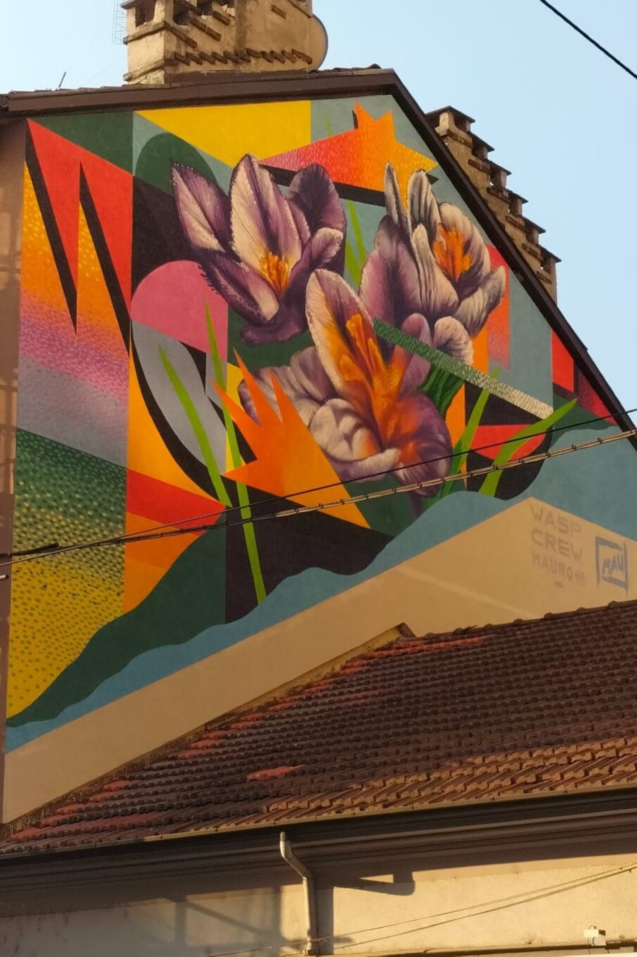 A work created by Wasp Crew, an artist duo formed by Edoardo Kucich and Gabriele Guareschi. It shows three purple flowers, providing natural imagery against a backdrop of colourful shapes. which are largely quadrilateral.