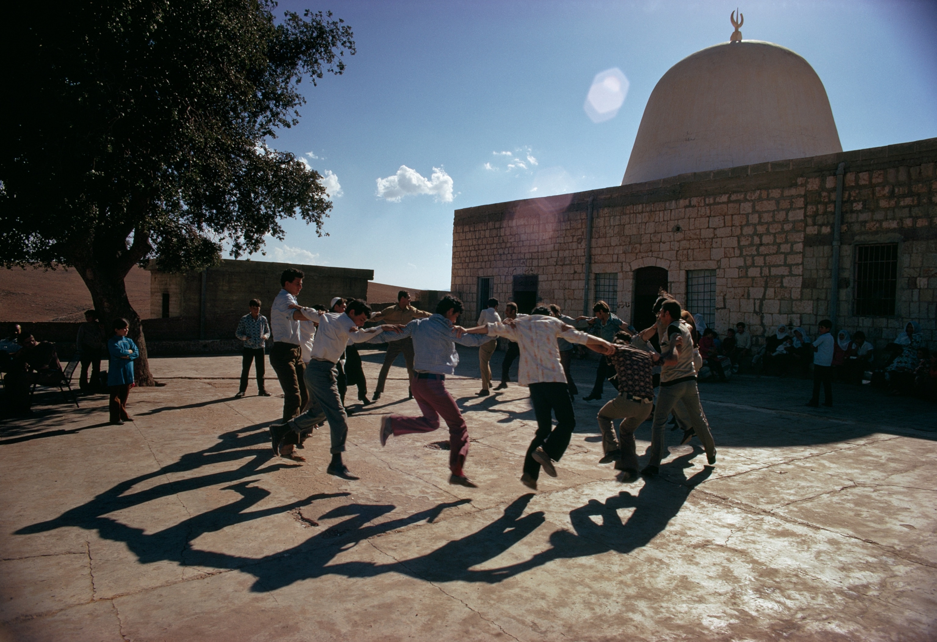 Young men dance in a ring beside a domed building, 1974