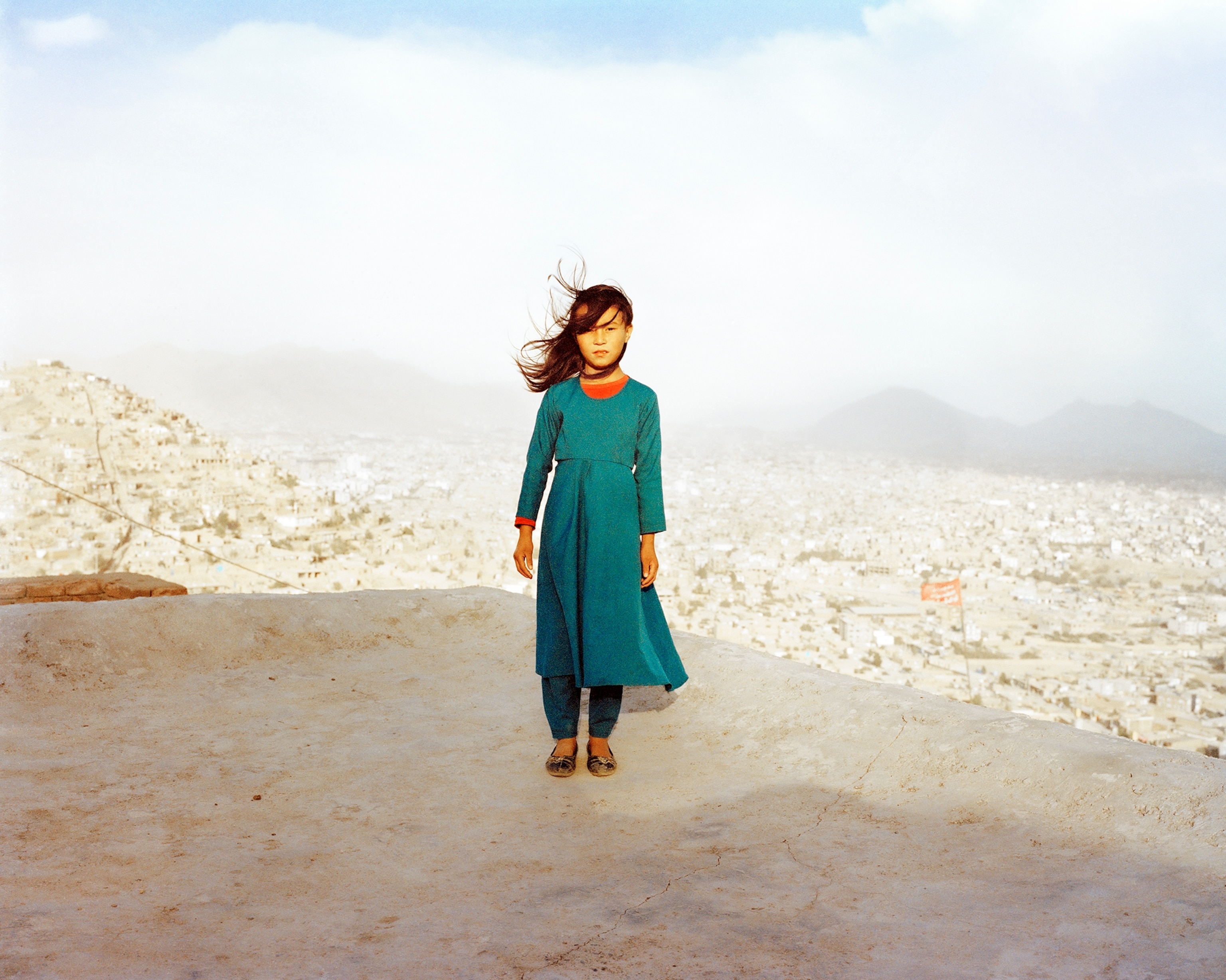 A young girl stands on the roof of the house with Kabul in the background.