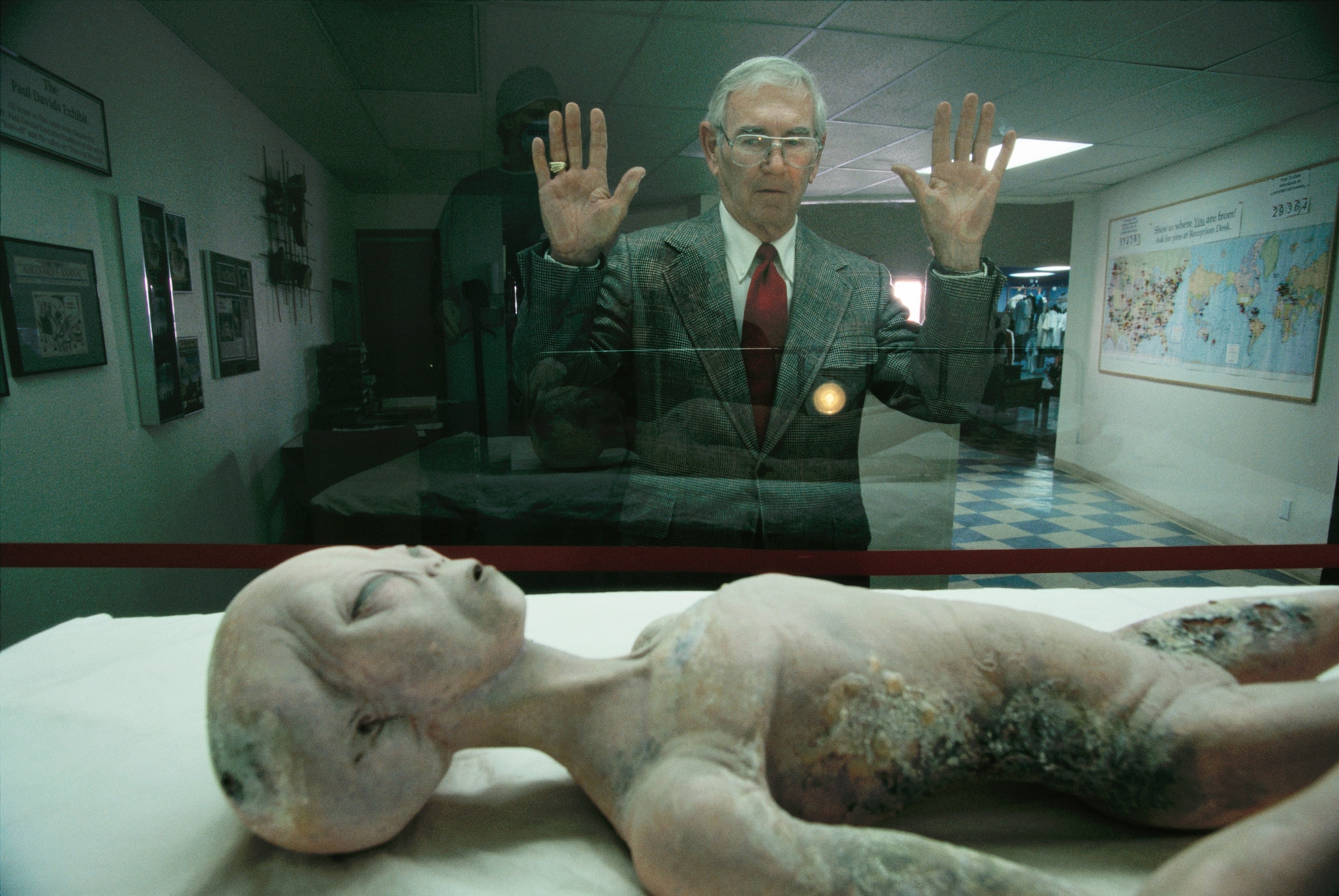 A man views an alien body through a glass showcase.