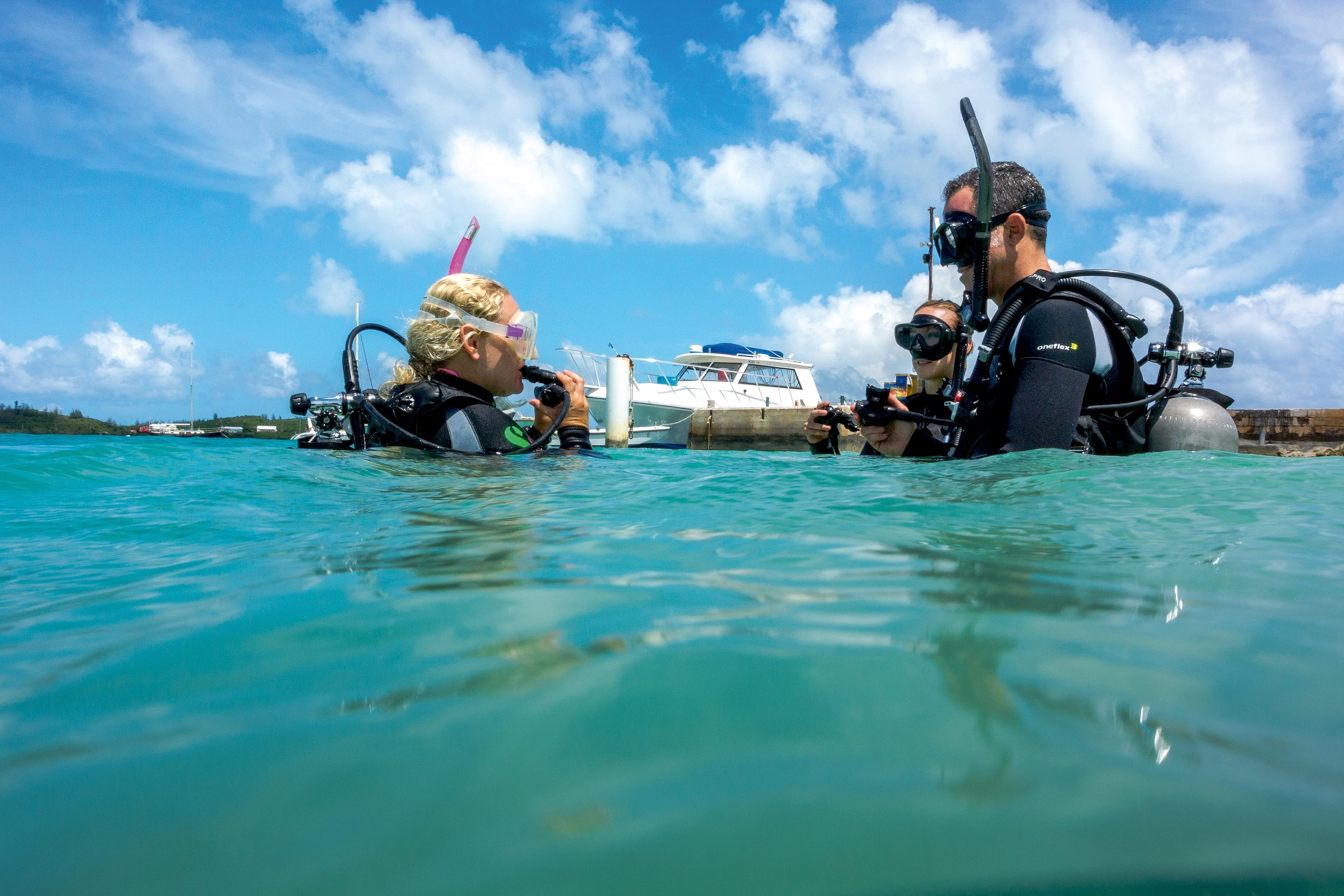 A group of divers half shown above water, getting ready to dive down into the ocean.