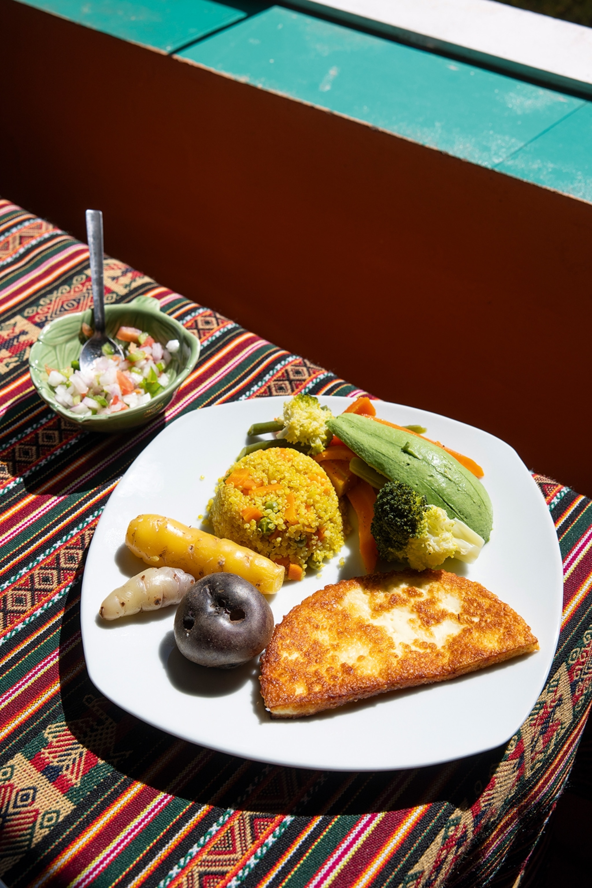 A close-up on a plate of food with boiled blue potato, jerusalem artichoke, avocado and a cheesy bread.