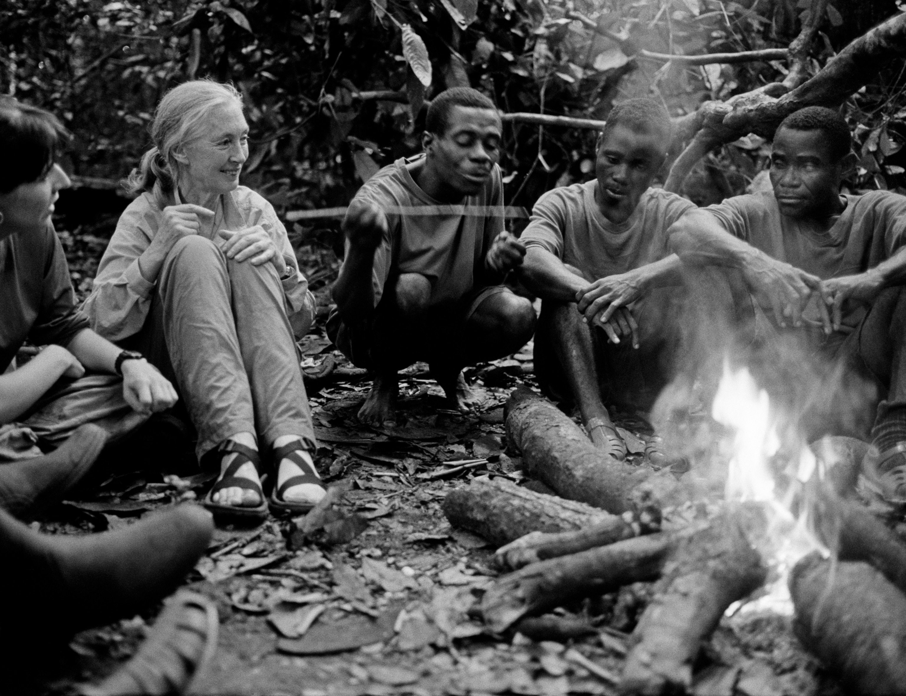B&W photo of the group on people around campfire looking at how one of them demonstrate monkey behavior.
