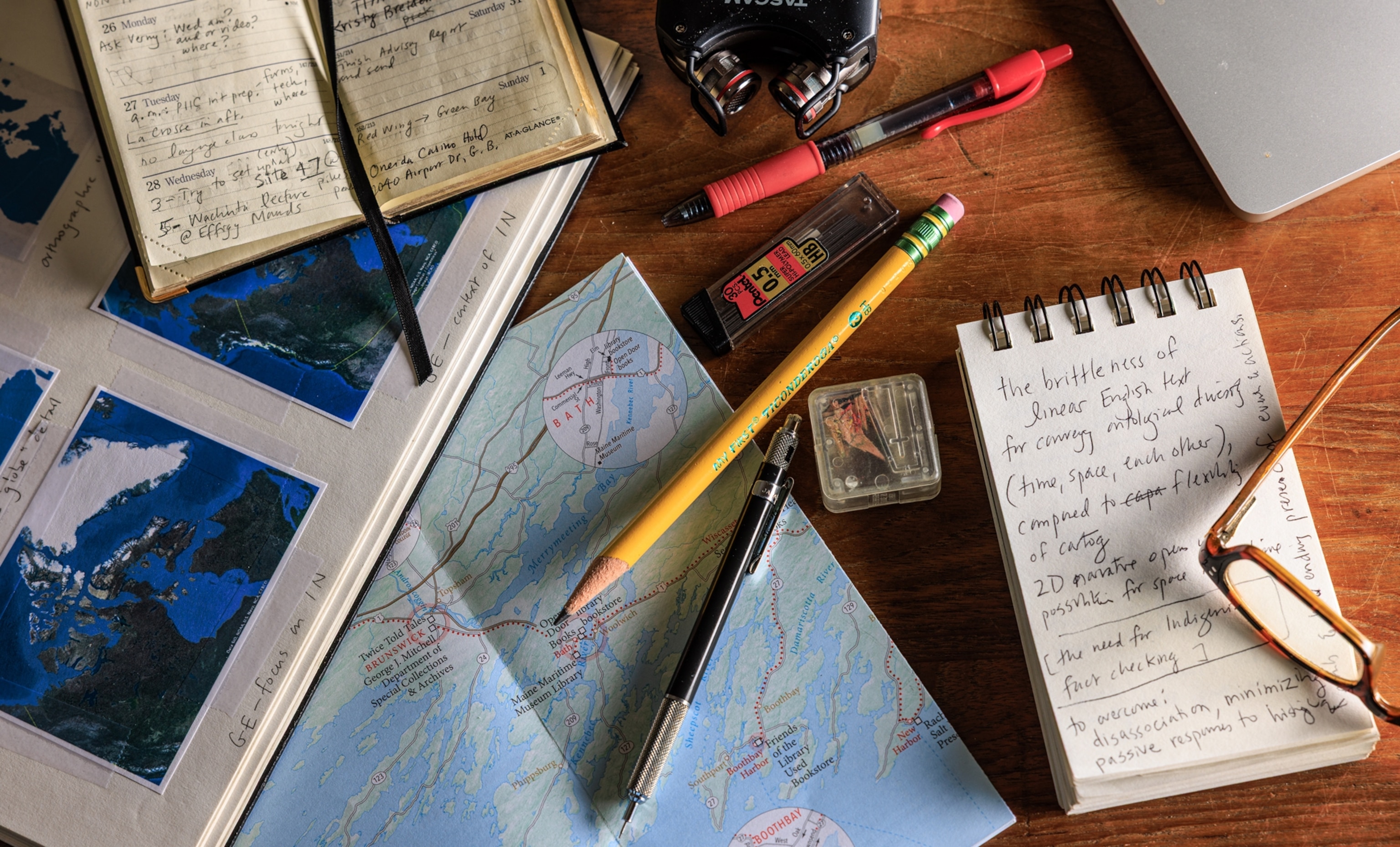 Maps, pencils, pens, and notebooks lay atop a table.