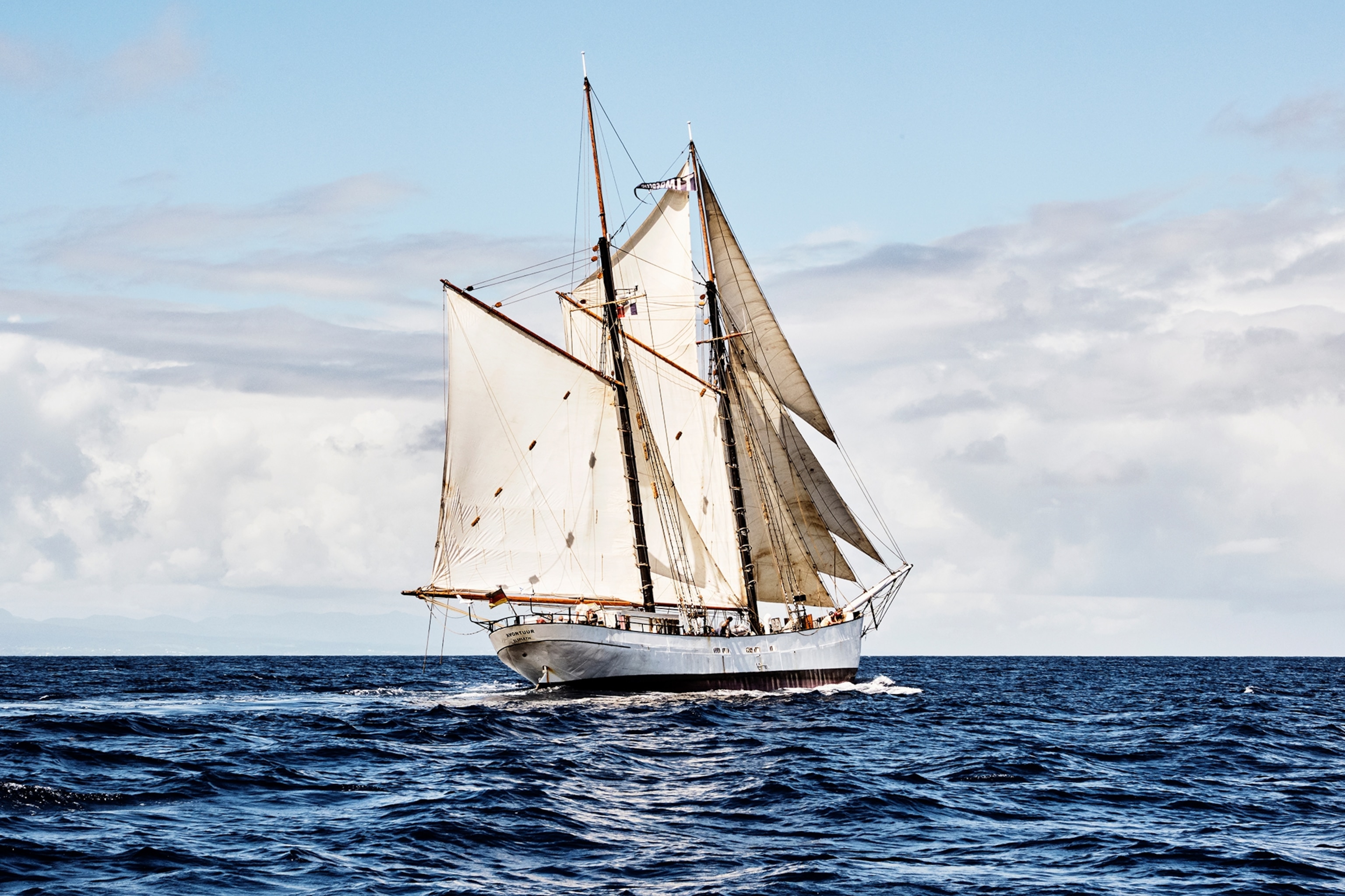 A sailing boat shown in full from the side while anchoring in the middle of the ocean.