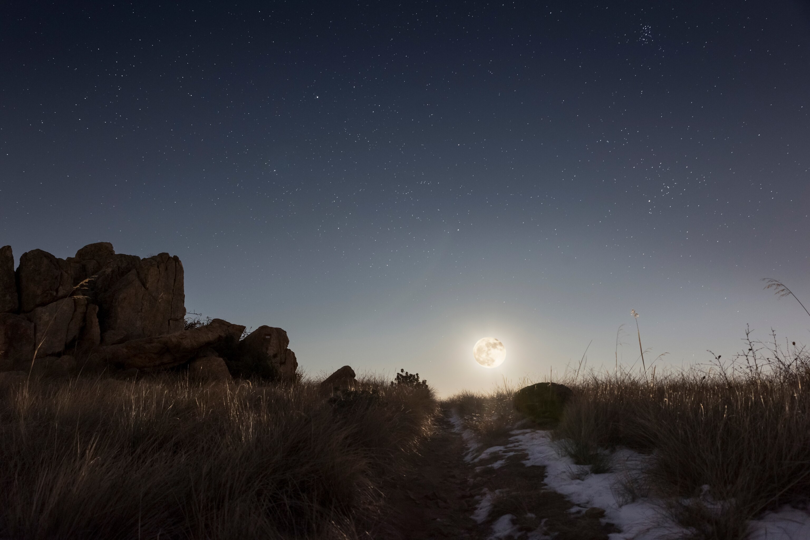 A full moon rises over a hill on a cold winter night.