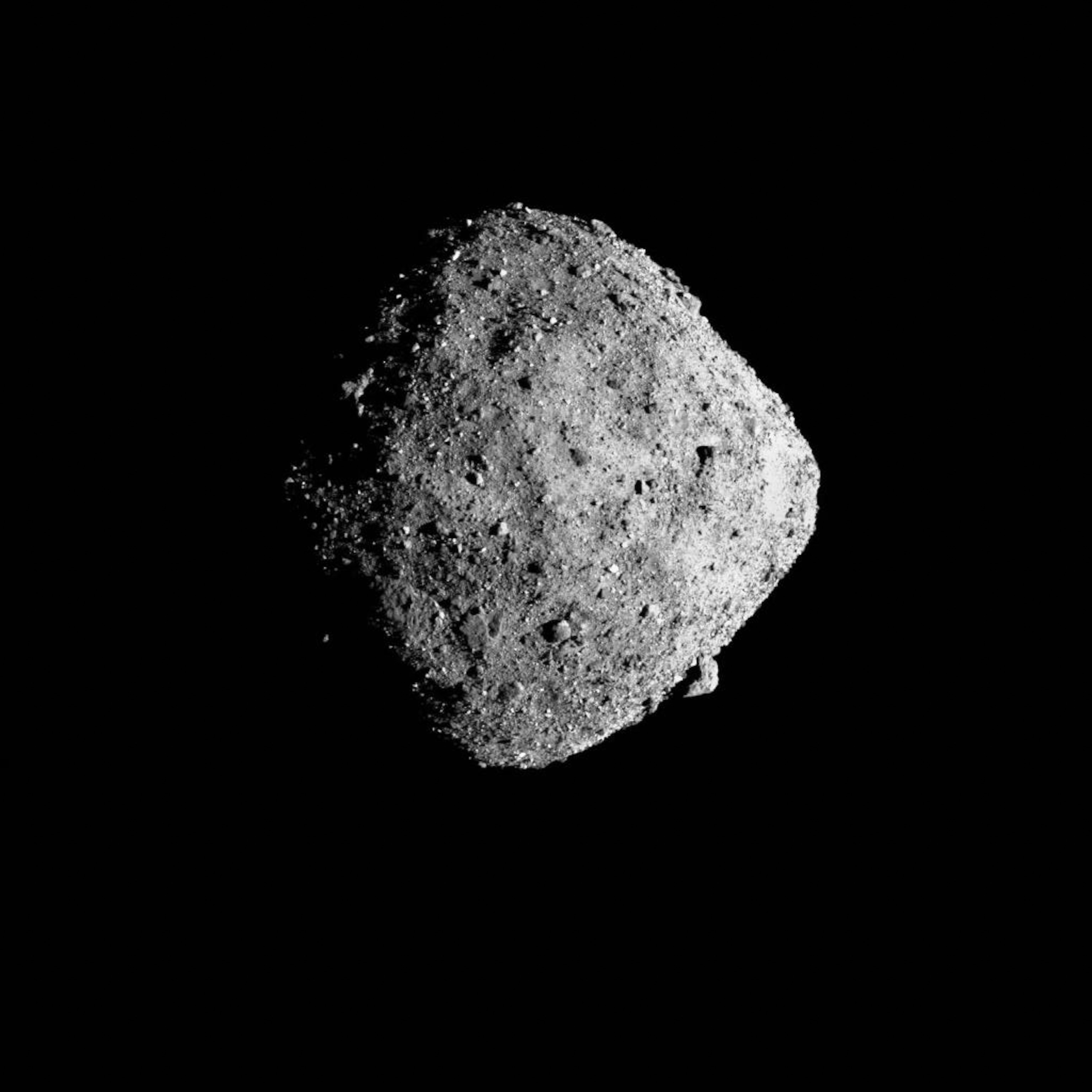 Black and white image of a rough, rocky asteroid in space against a stark black background