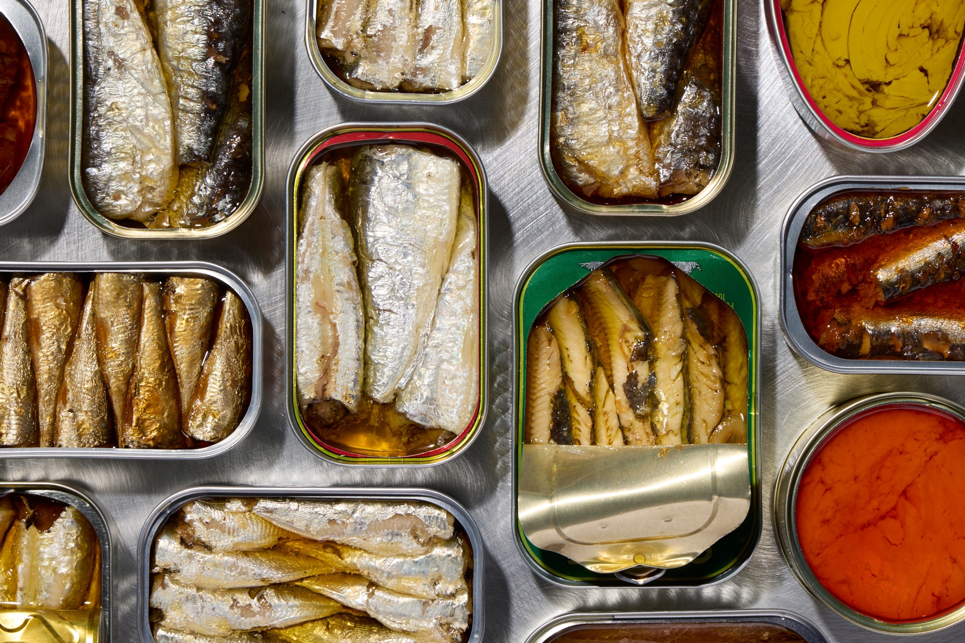 Various types of tinned fish lay in a grid pattern, some open some closed.