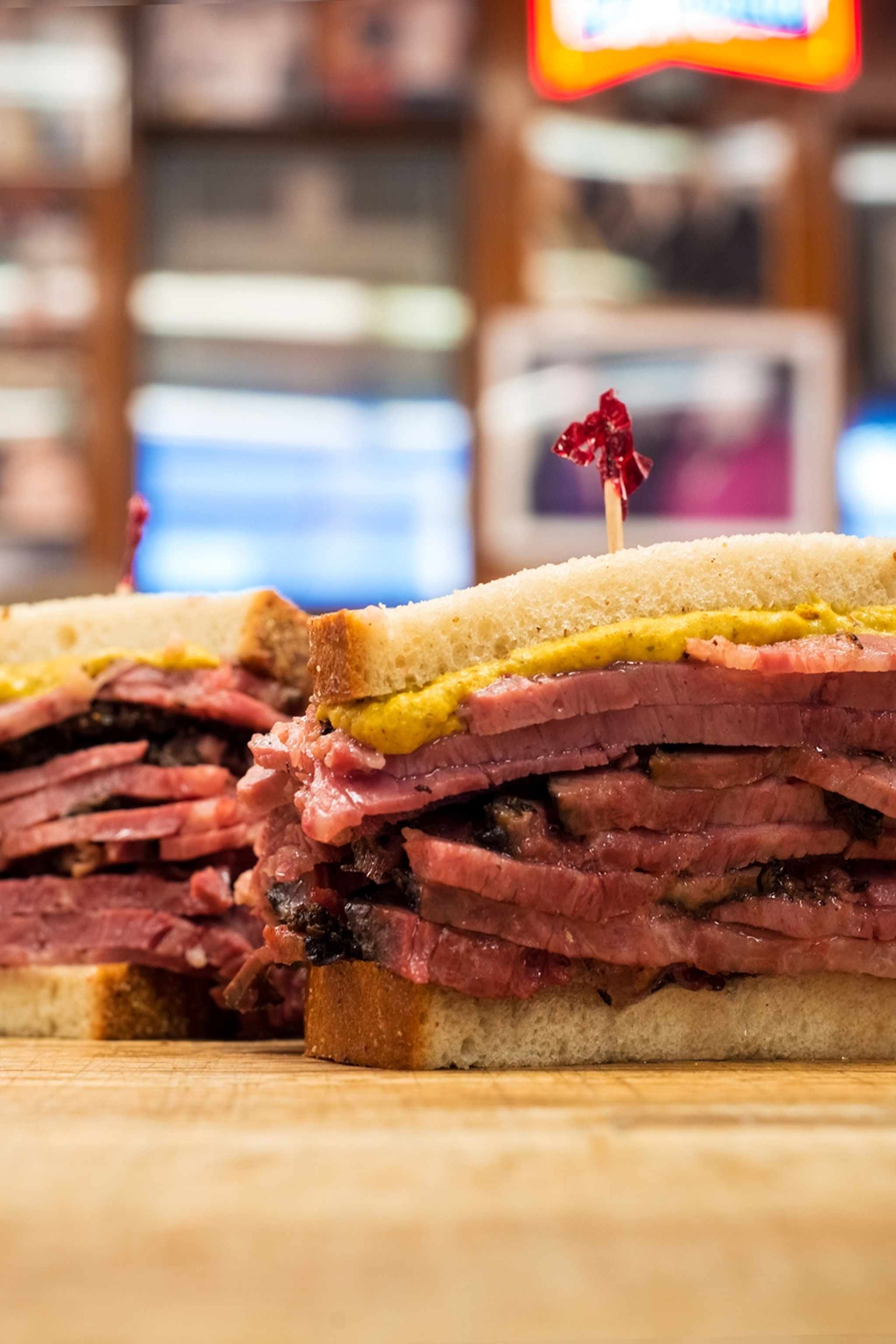 A stacked sandwich cut in half, revealing multiple layers of pastrami meat topped with mustard.