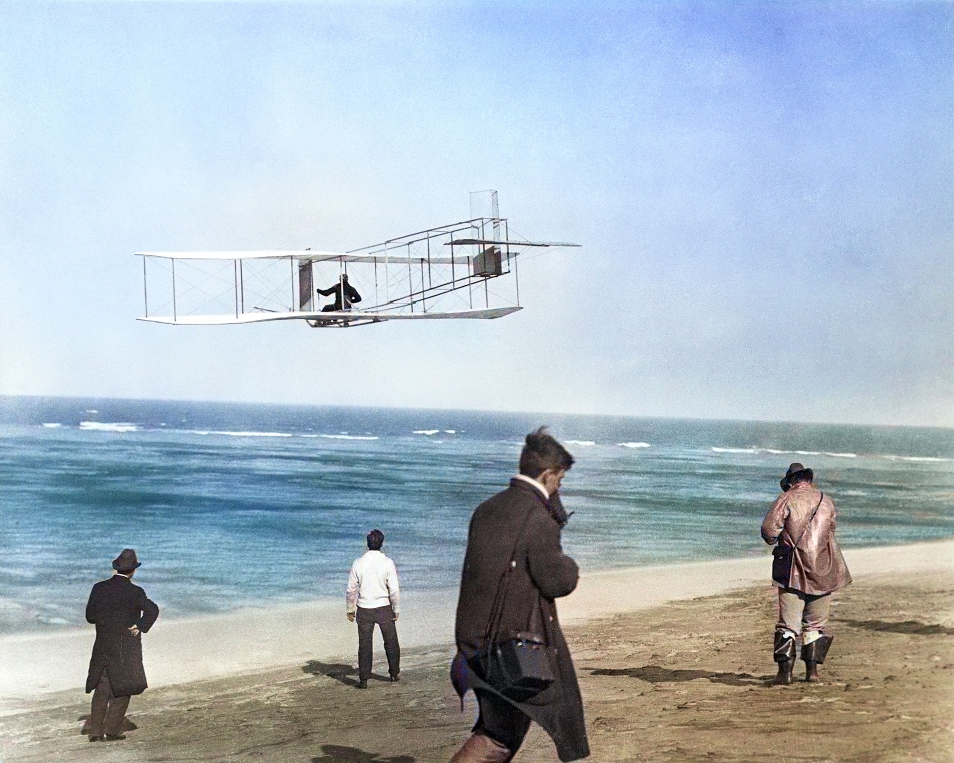 In this colorized version of a 1911 photo, one of the Wright brothers soars over the surf near Kitty Hawk, North Carolina, where they began experimenting with gliders in 1900.