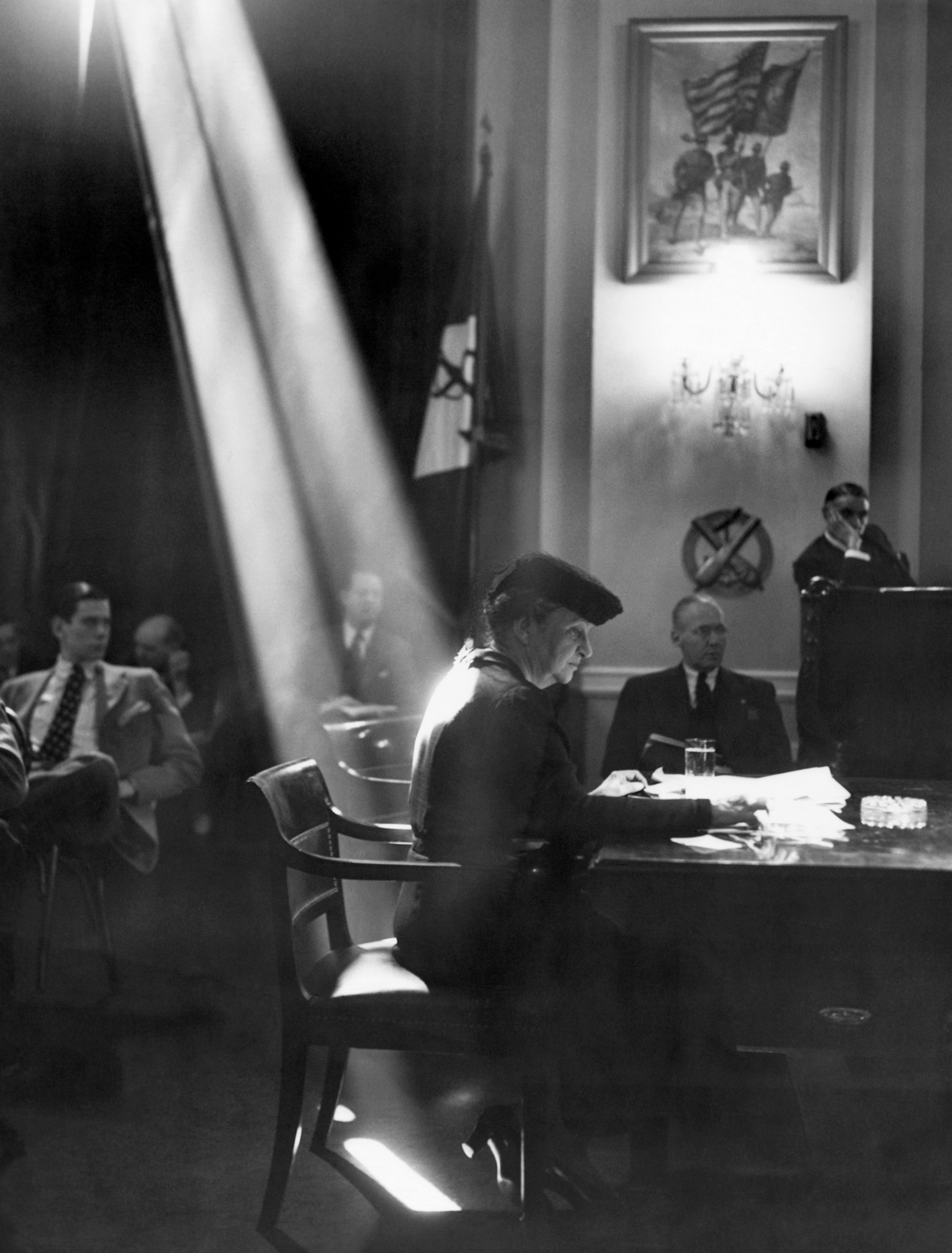 A shaft of light falls on the back of Secretary of Labor France Perkins as she testifies before the House Naval Affair Committee.