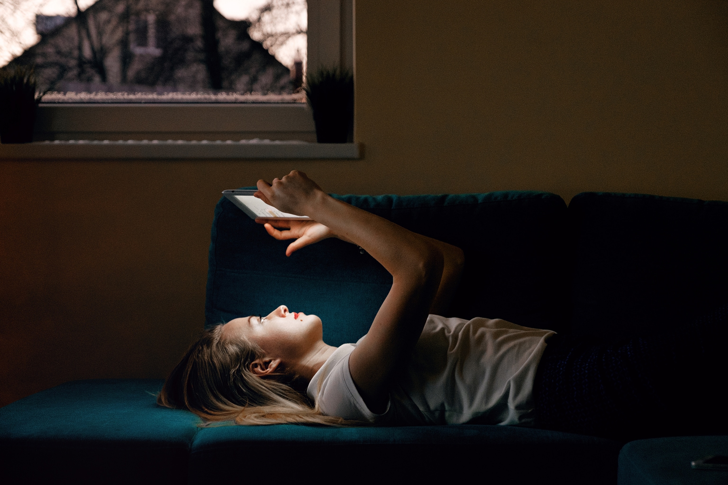 Side view of young blonde lying on sofa with tablet.