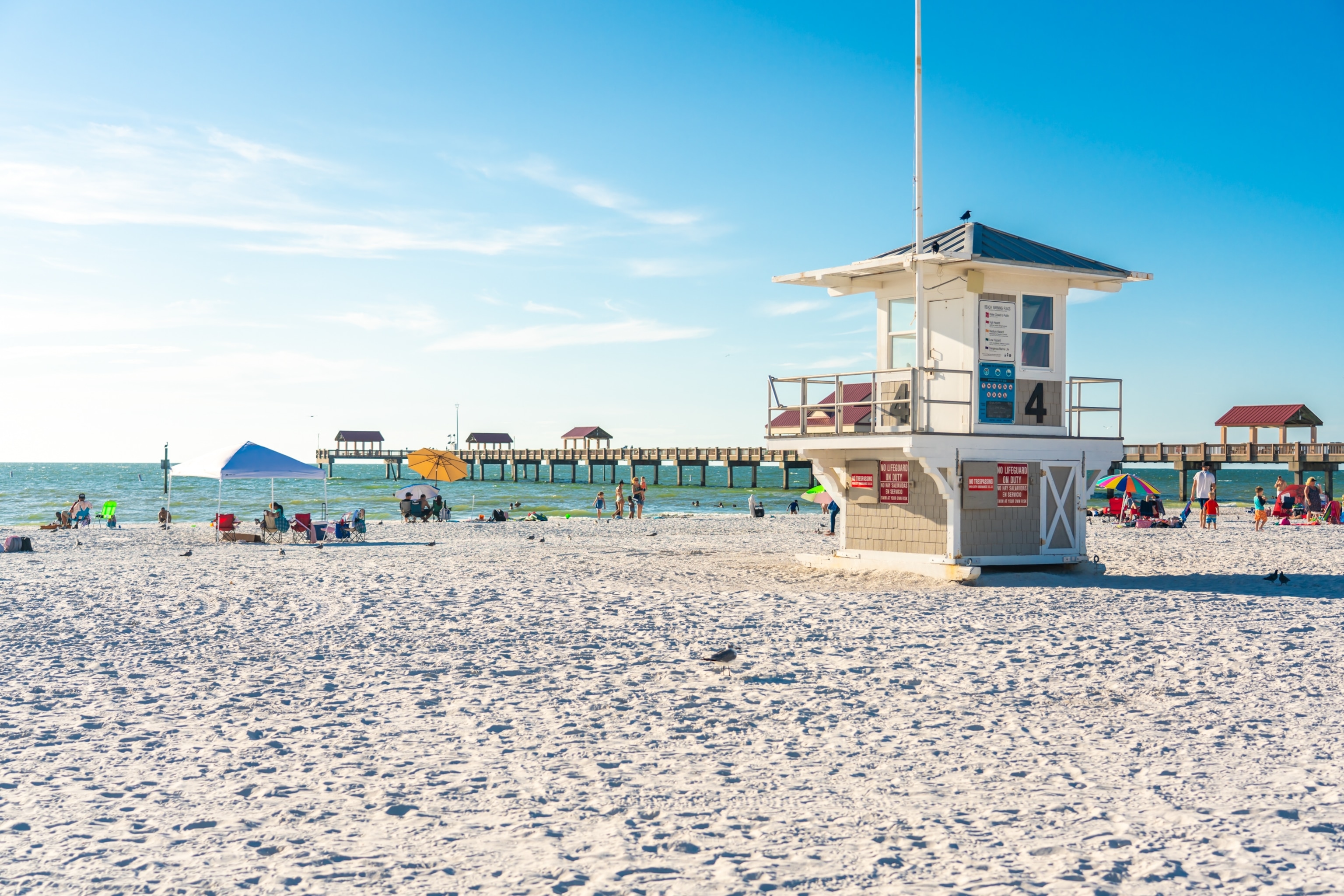 White sand beach with a wooden pier stretching out into the turquoise sea, and a wooden elevated lifeguard hut stood in the foreground