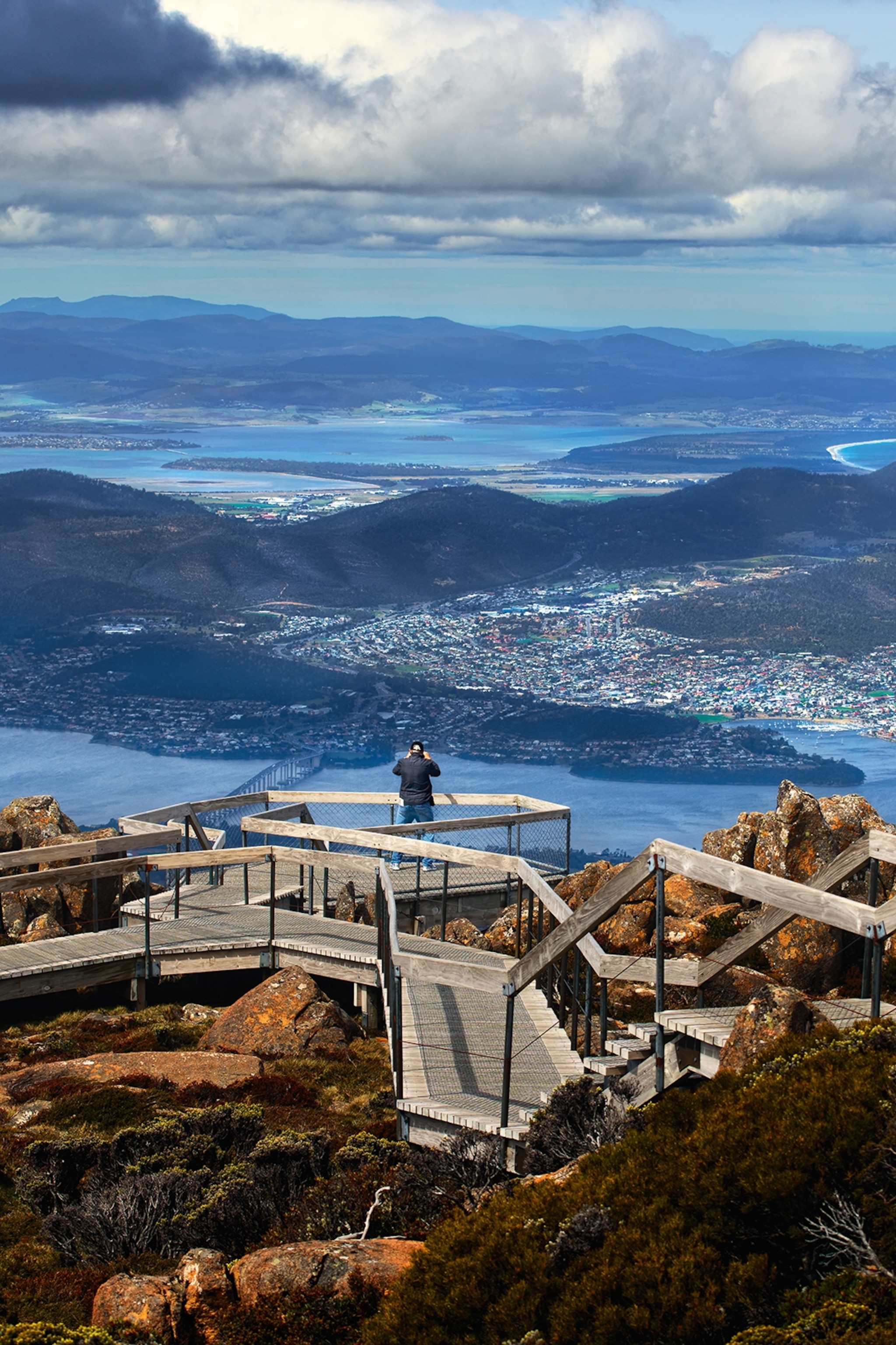 A boardwalk on the top of a mountain with a view of a seaside city and hills.