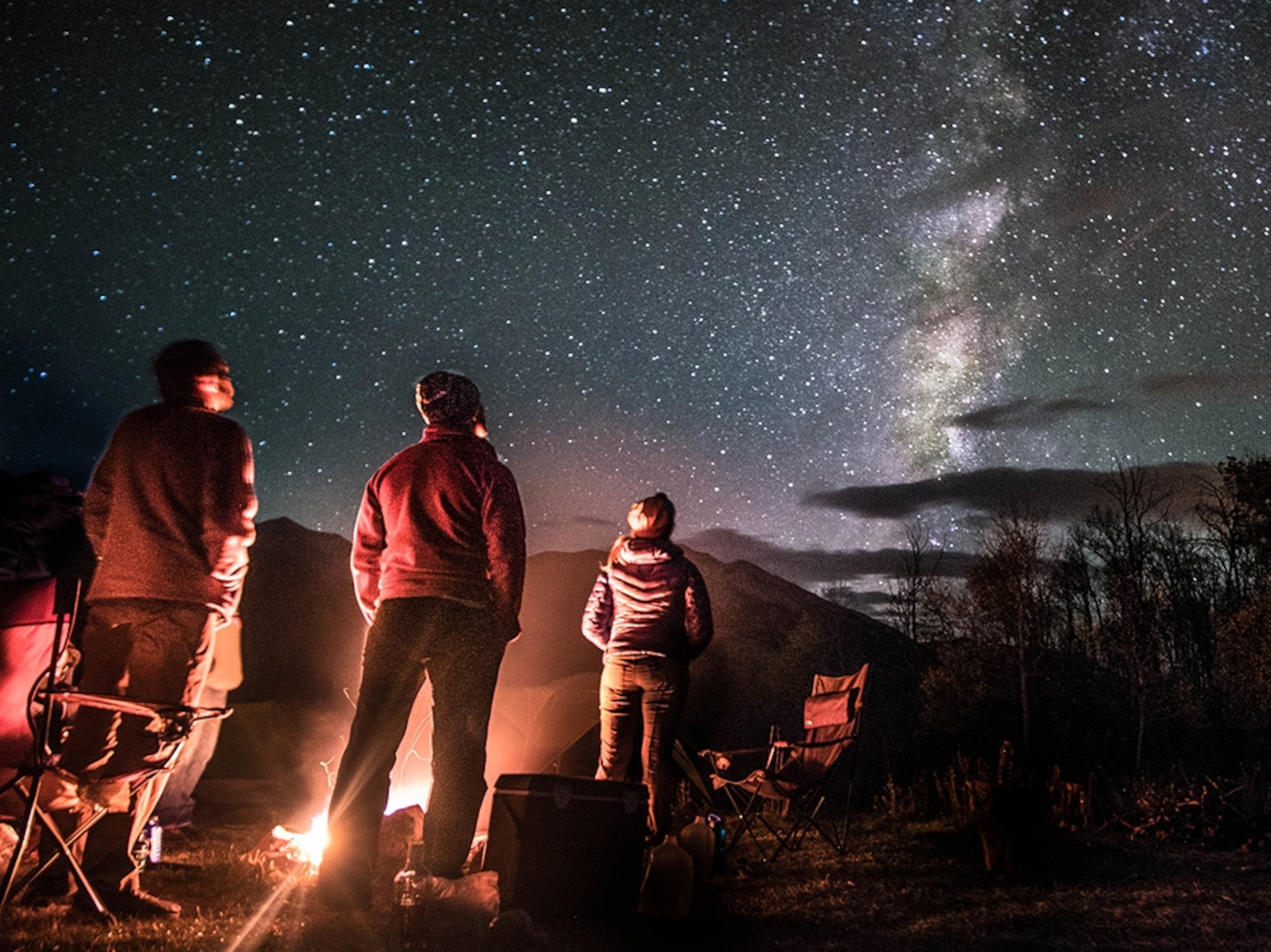 a group of campers standing around a campfire at night
