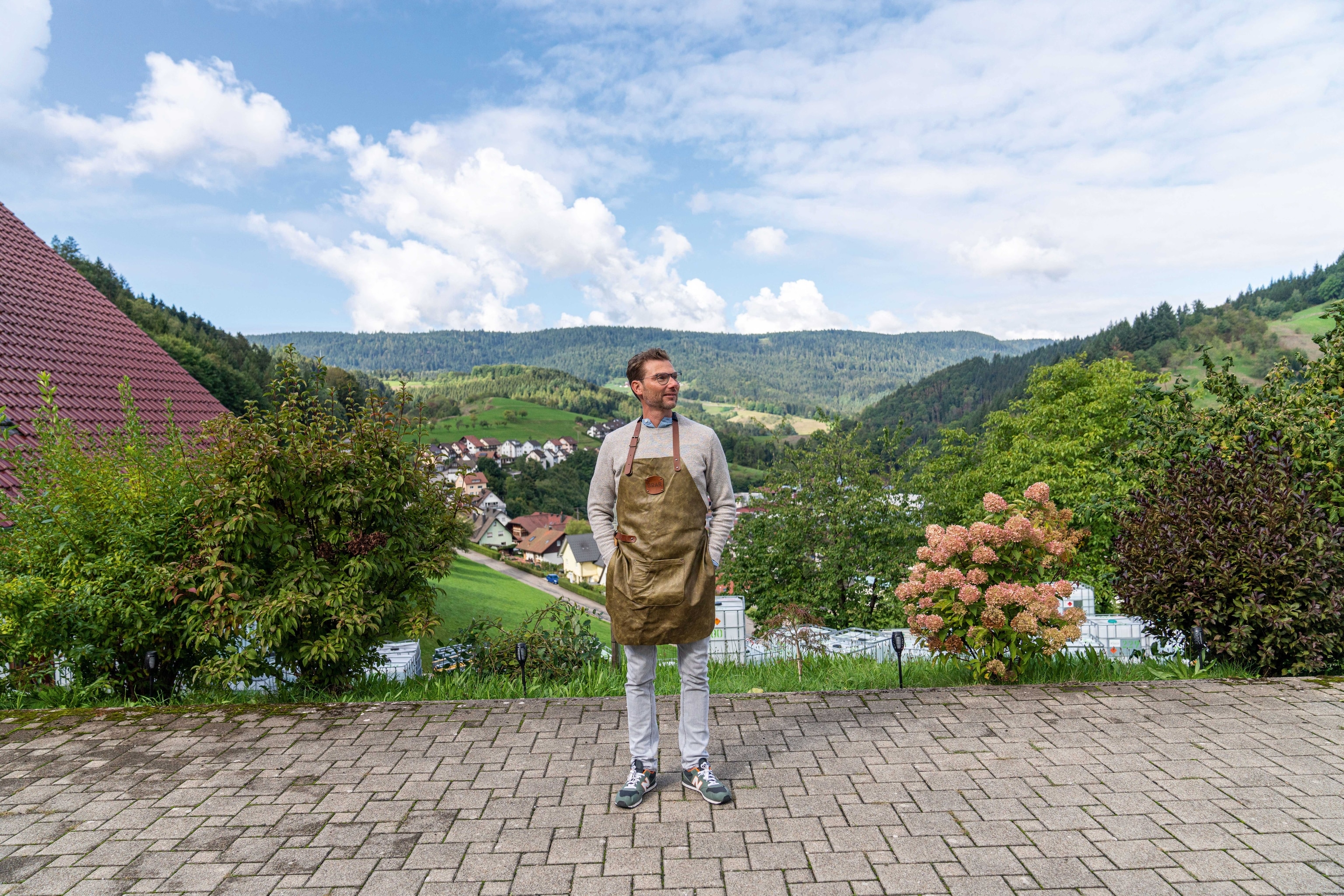 Hannes Schmidt stands in front of the Boar Distillery amid lush green hills.