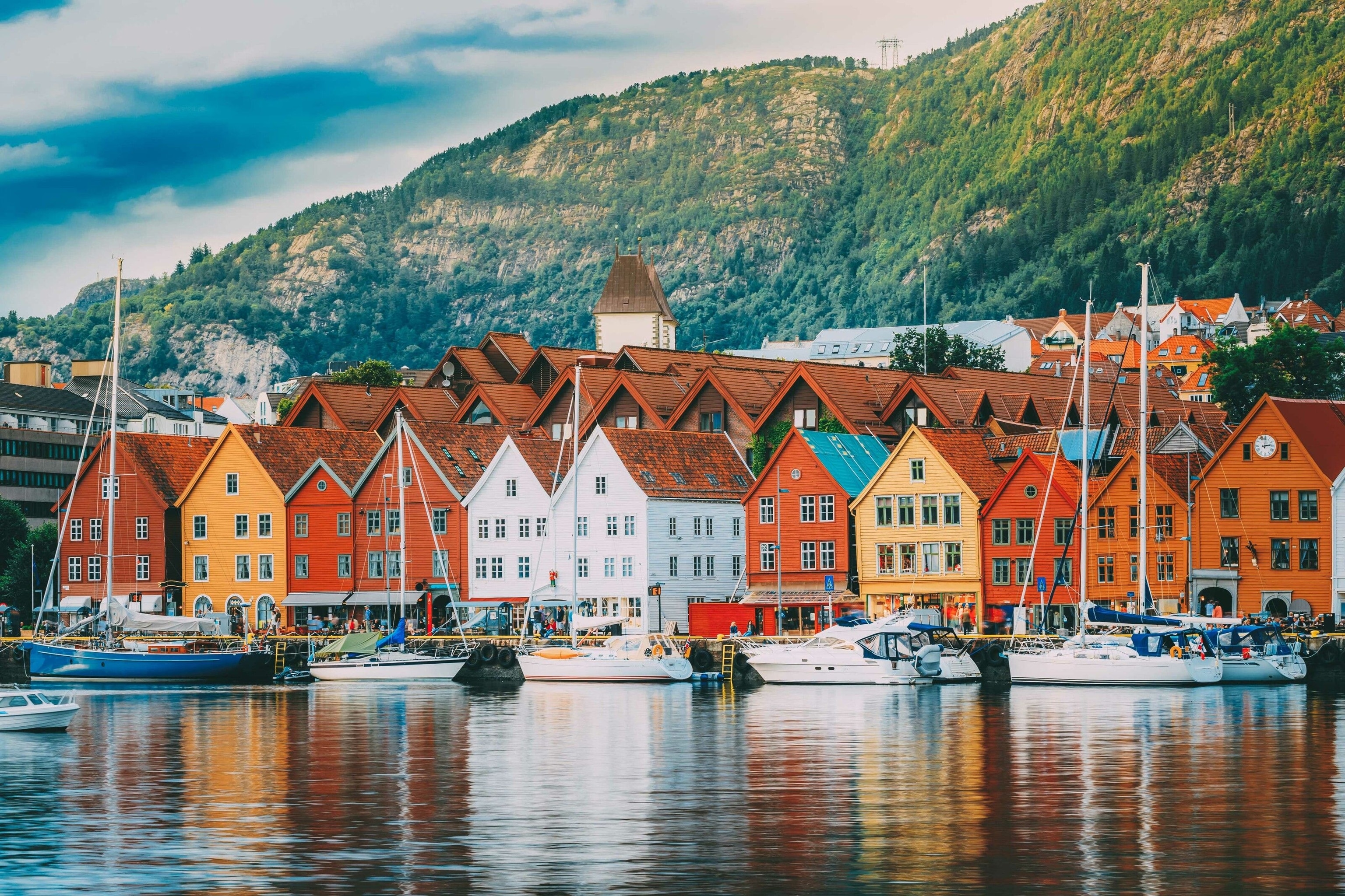 Red, white and yellow houses in a line. Boats are moored in front of them.