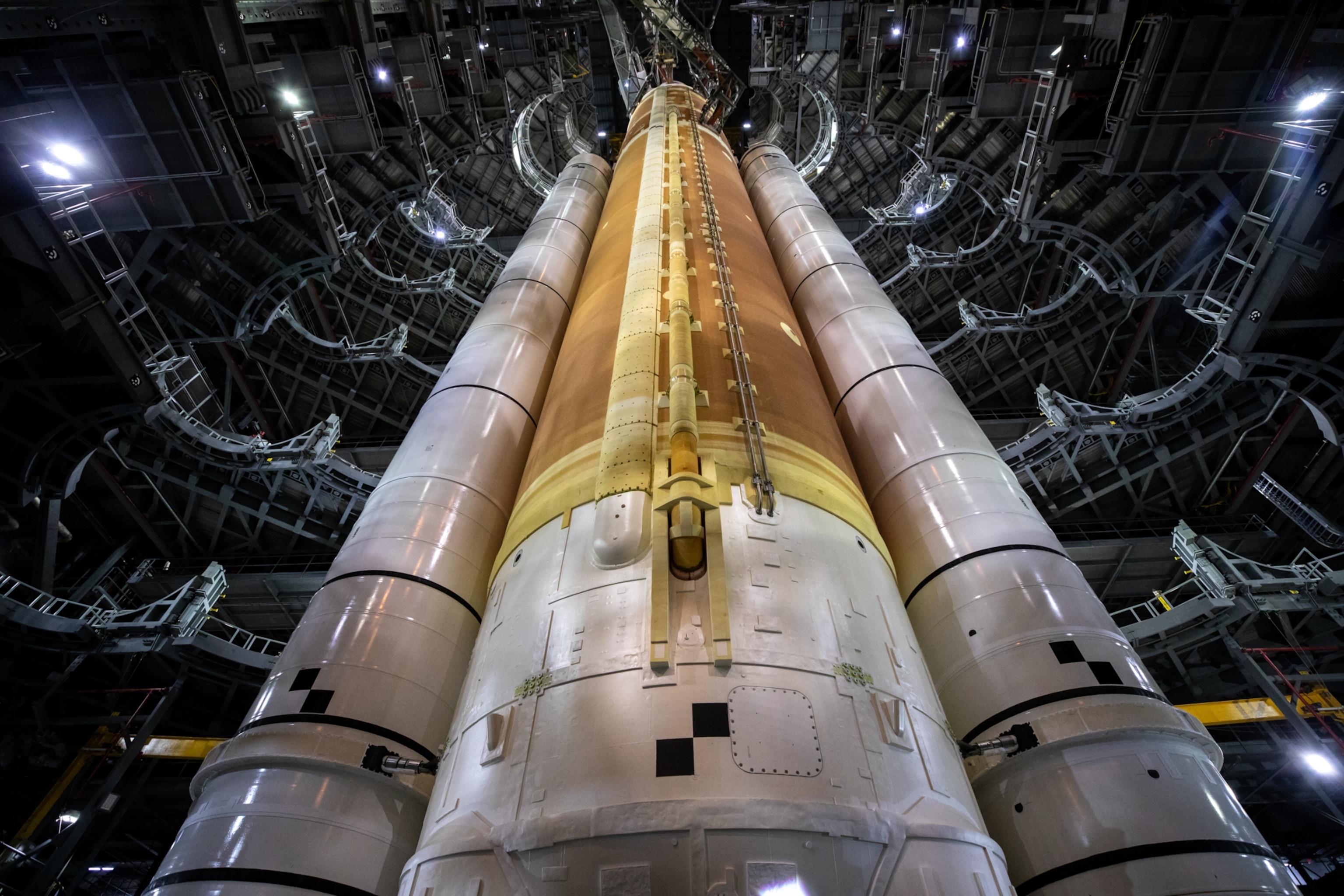 Upward view of a large rocket inside a hangar, flanked by metallic structures.