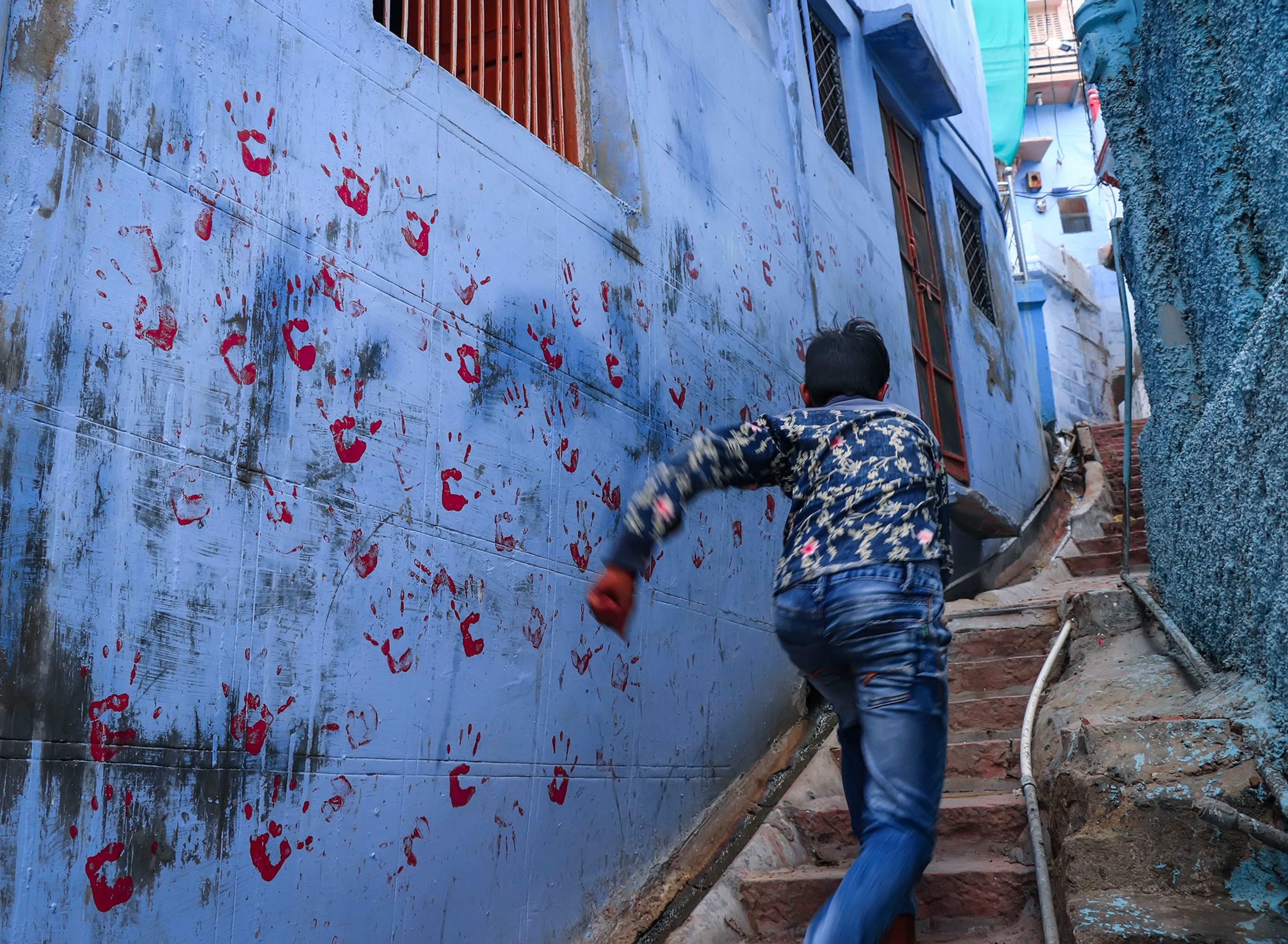 a child running up blue walled stairs with red hand prints