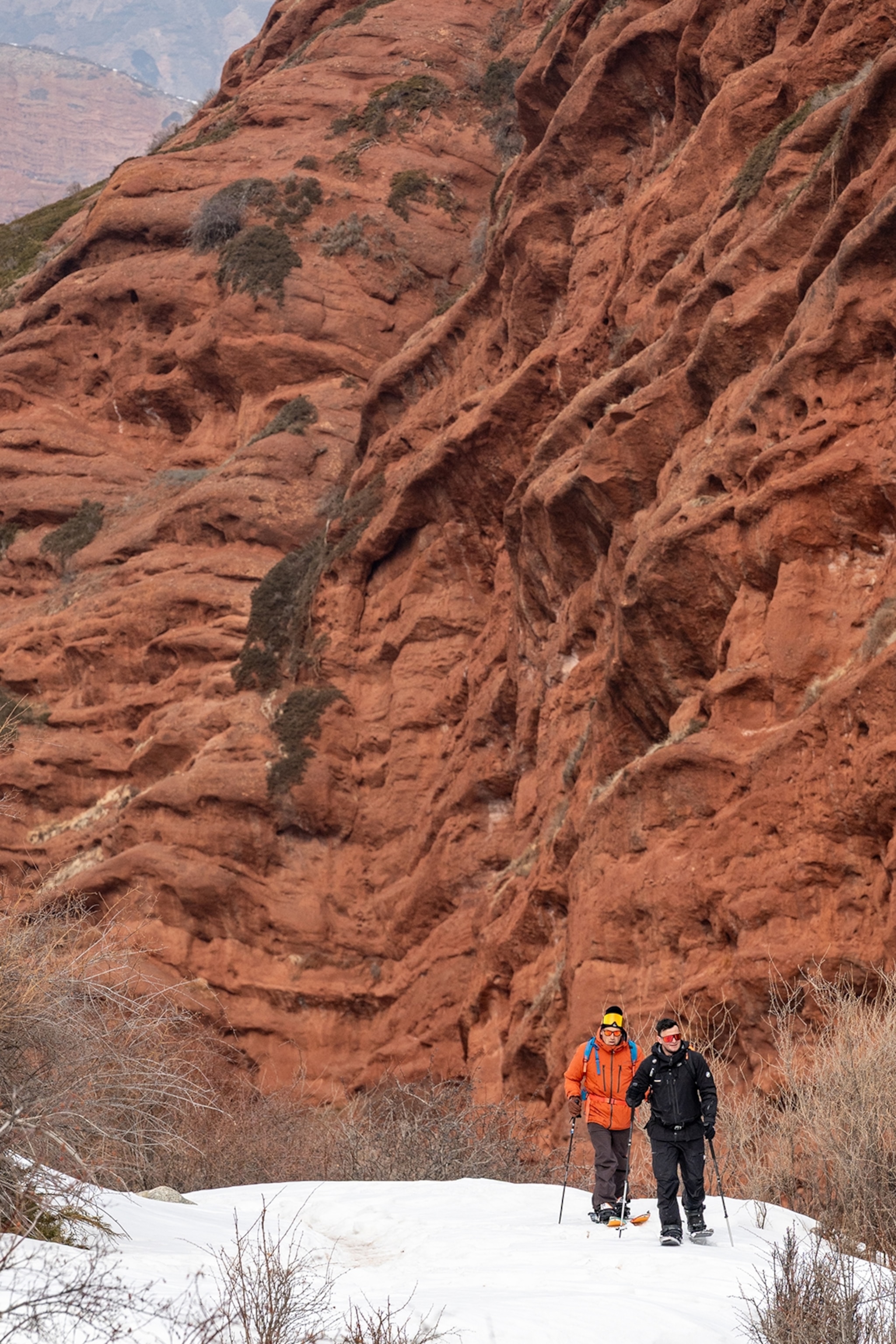 A stone valley with two hikers walking past a textured wall in the snow.