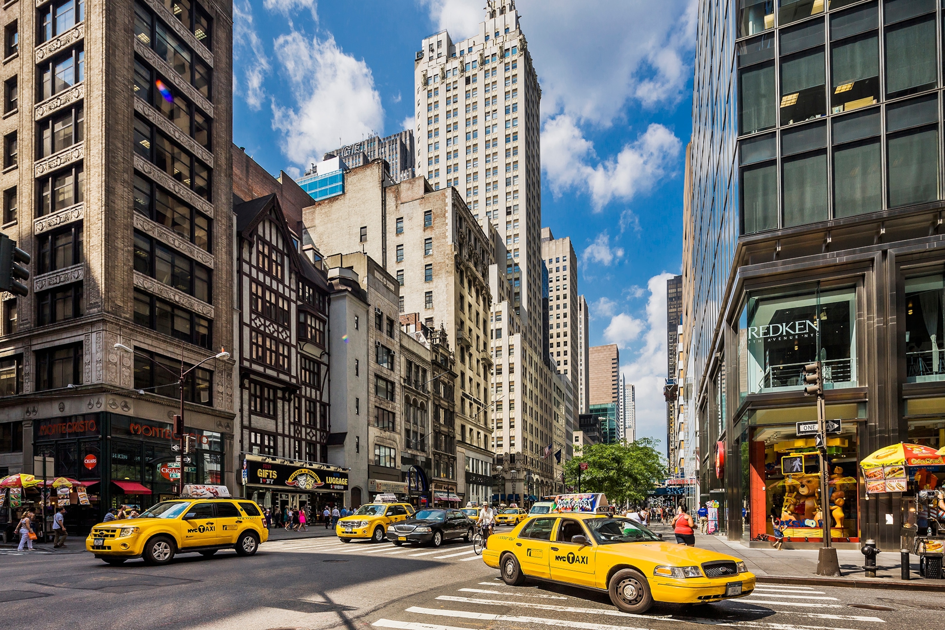 Crossroads in a city surrounded by high rise buildings and yellow taxis driving on the road