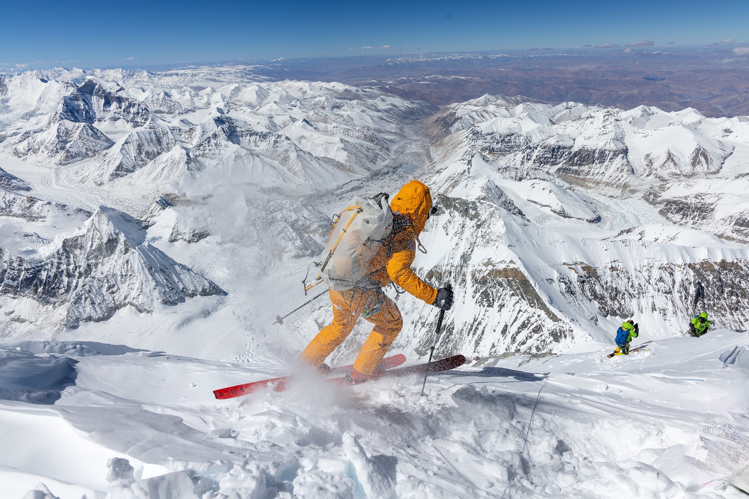 Skier wearing yellow suit descends down the snowy mountain