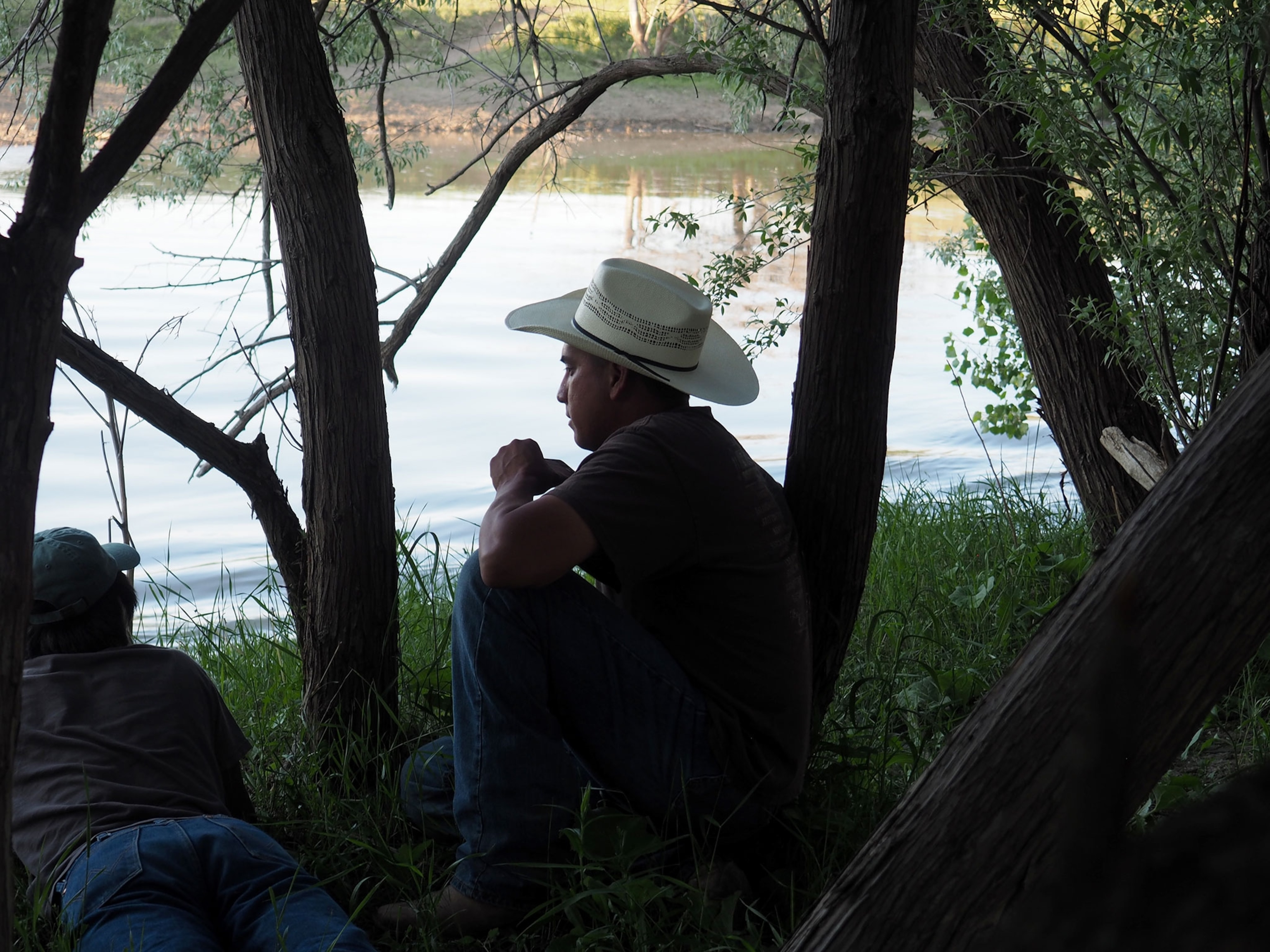 a young man in a cowboy hat sitting by the river on the Crow Indian reservation