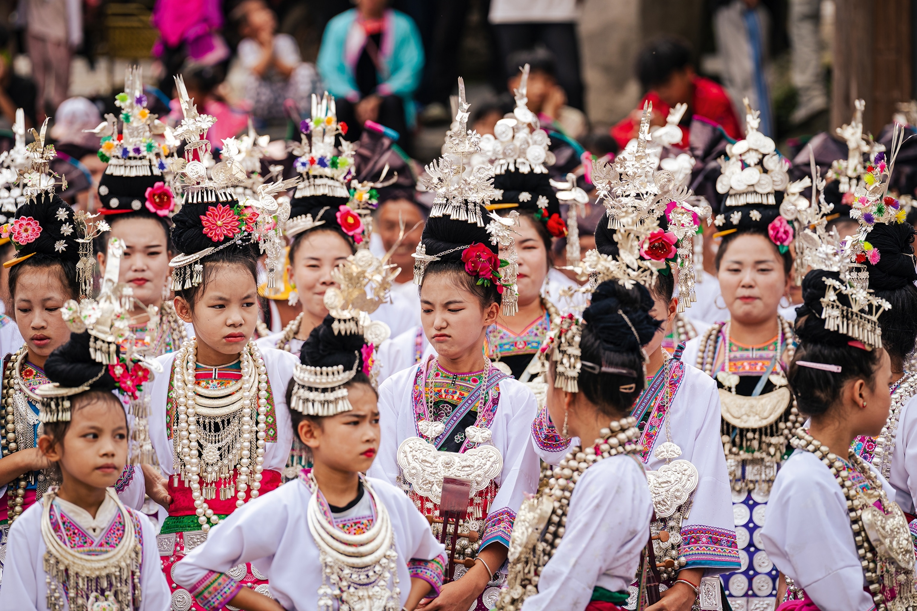 A crowd of young Chinese girls in traditional dress and head pieces performing a song.