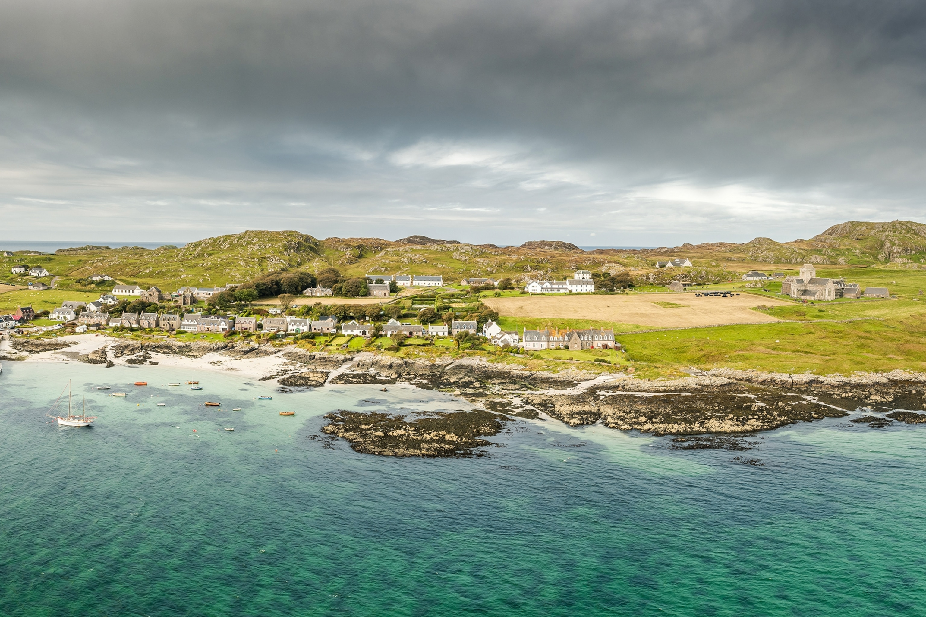A rugged yet shallow coastline with small boats anchored in clear waters and a row of houses facing the sea.